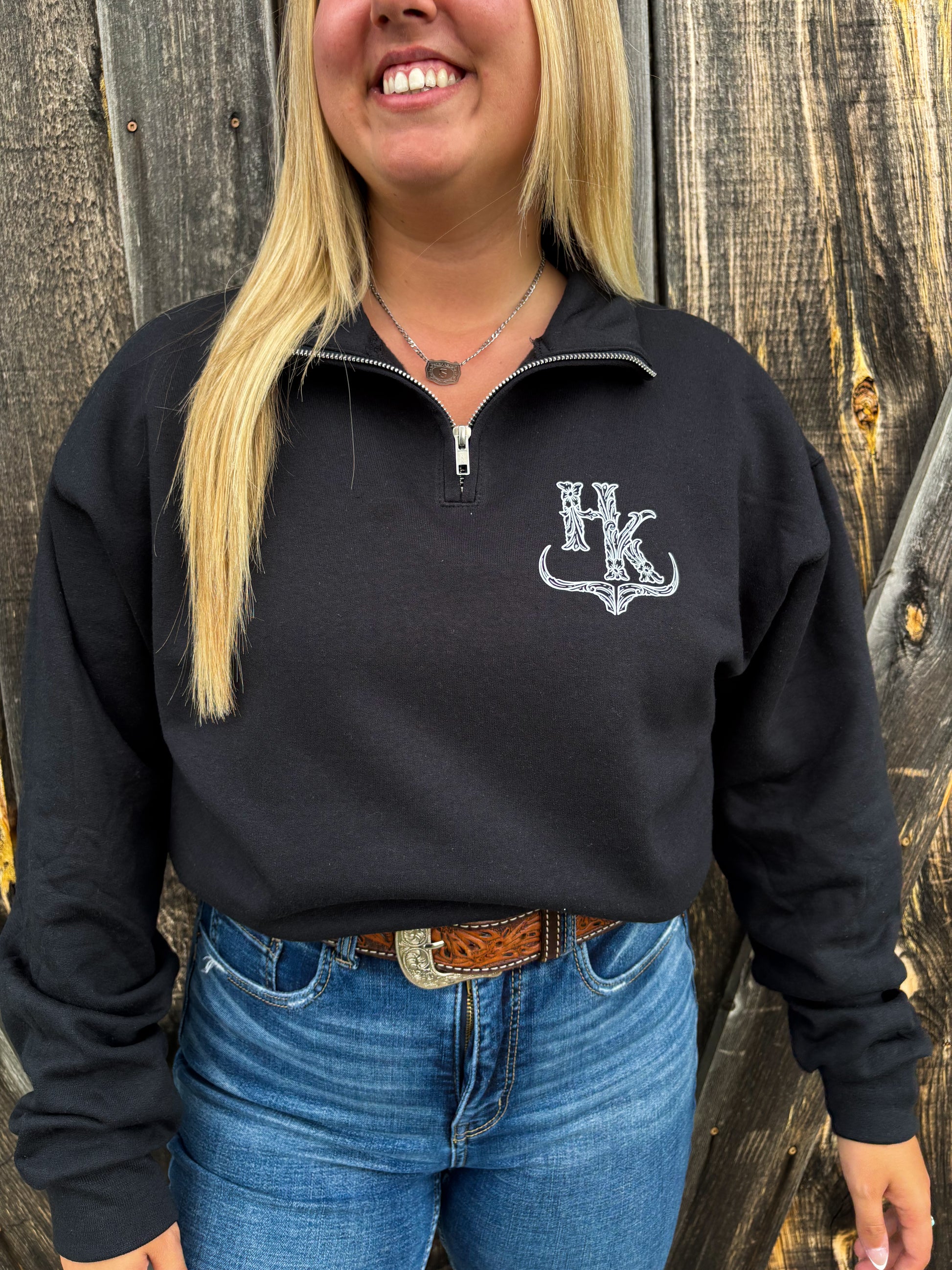 Close up of a woman wearing the Hides & Kinds black brand quarter zip with white logo design