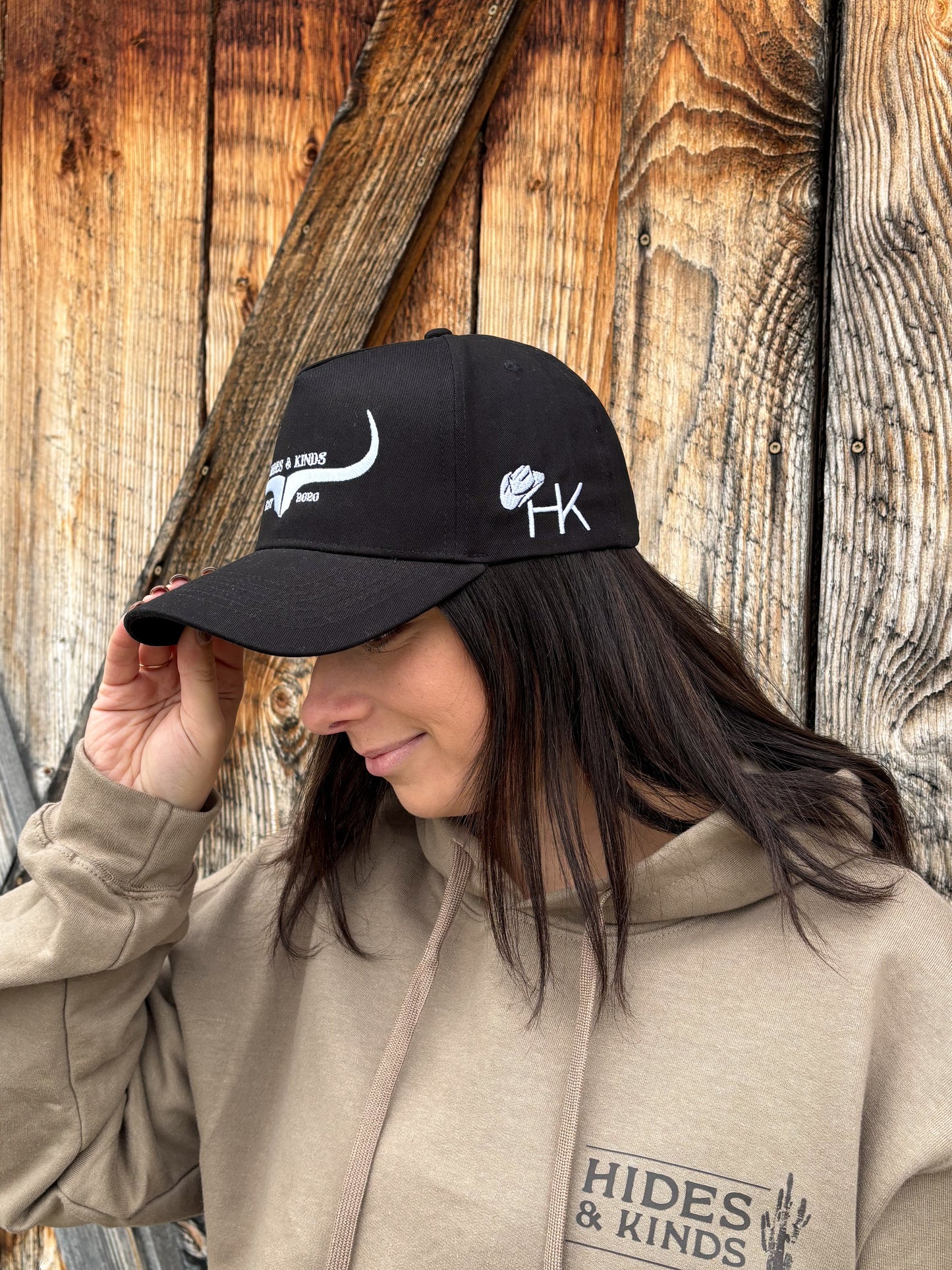 Side profile of Hides & Kinds Original Logo Hat in black and white with embroidered HK logo, styled on female model.