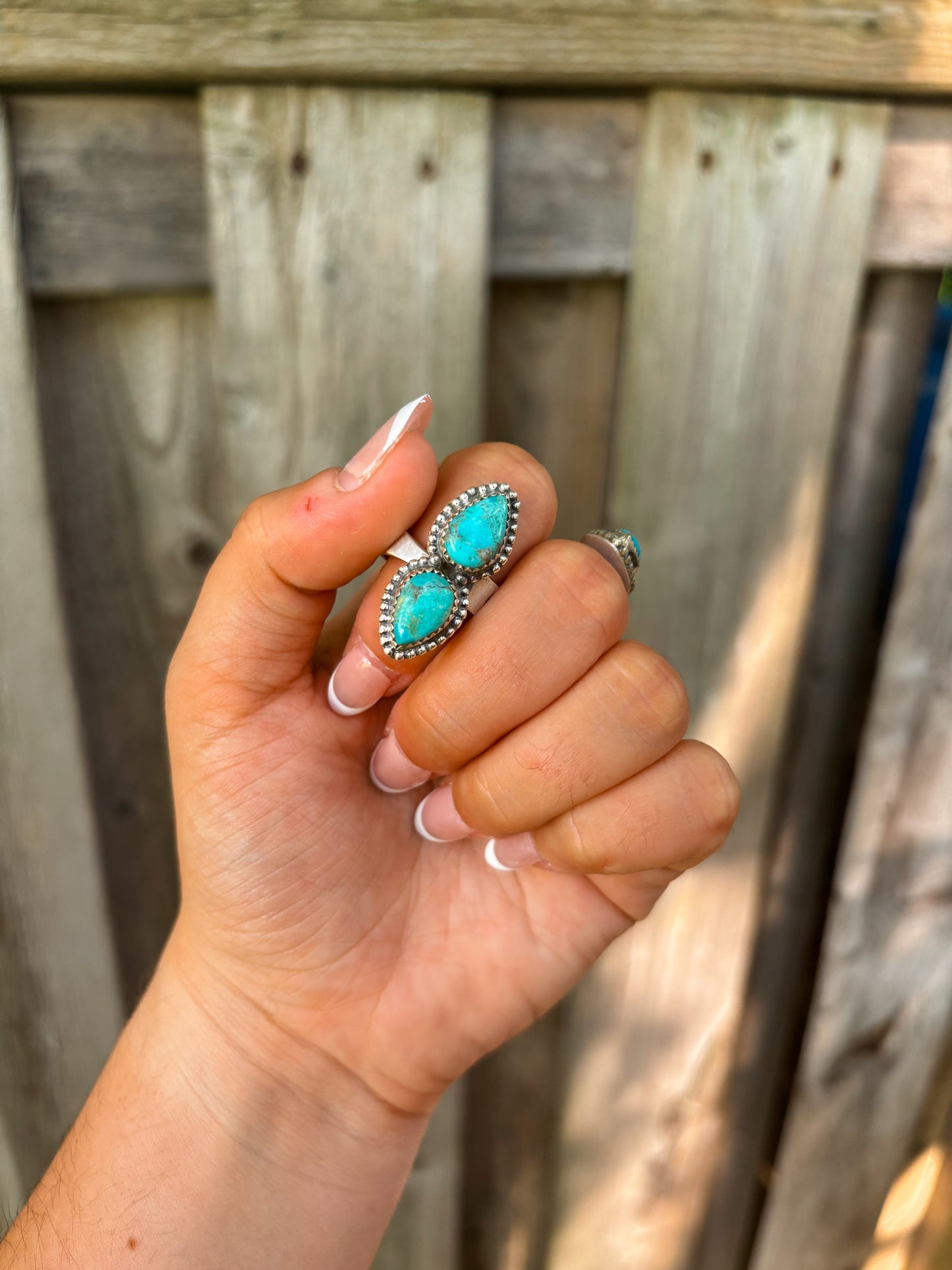 Adjustable turquoise ring with two genuine stones shown outdoors with wood background.