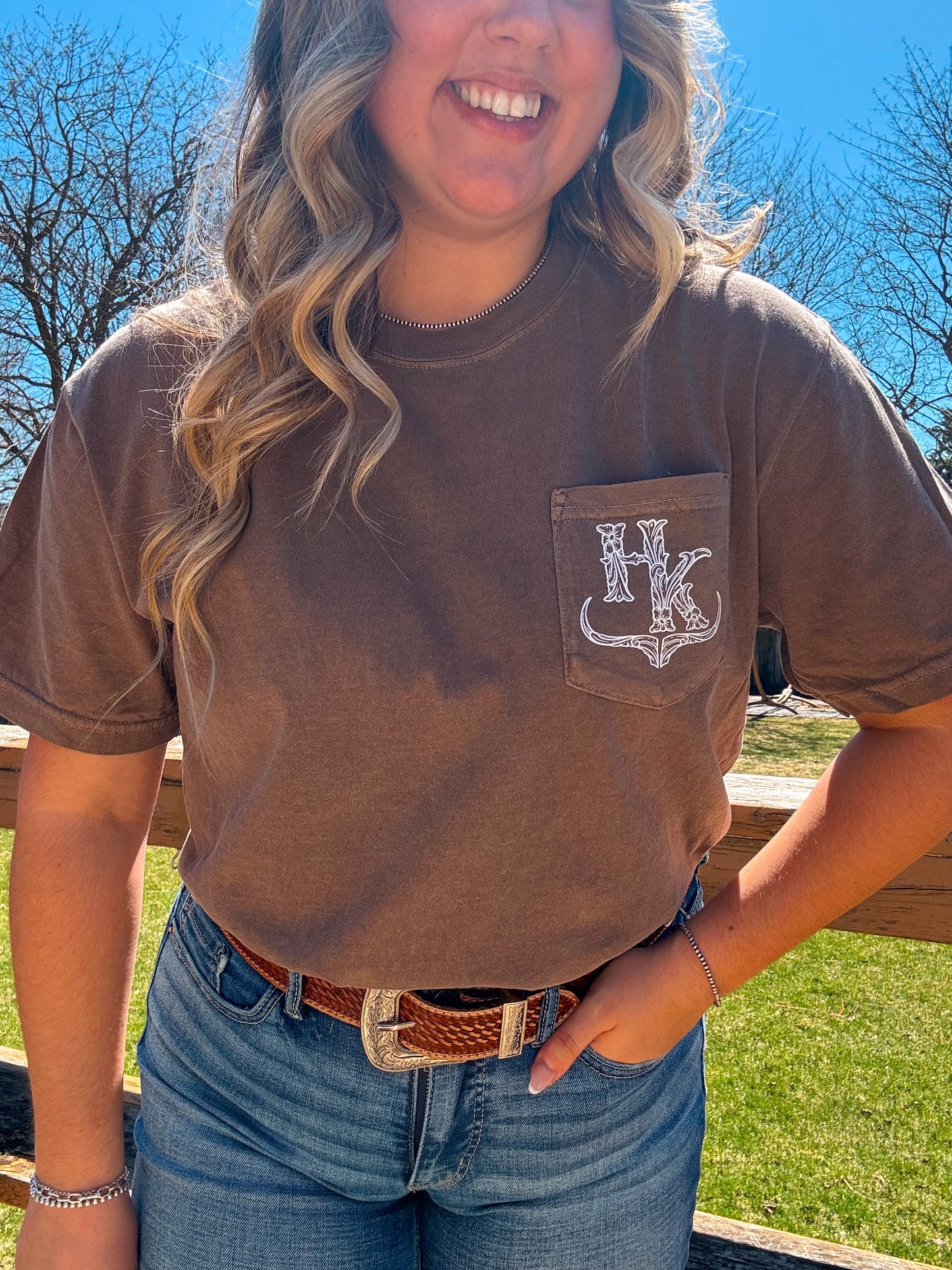 HK Branded Pocket Tee in espresso brown photographed outdoors in natural light, showcasing the pocket and logo detail.