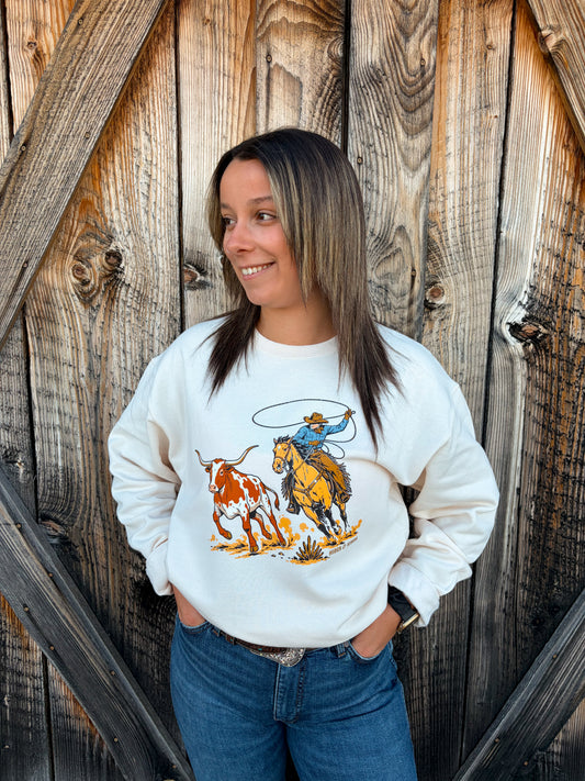 Front view of the Hides & Kinds Breakaway Crewneck in cream, showing a colourful western graphic of a cowboy on horseback swinging a lasso beside a running longhorn.