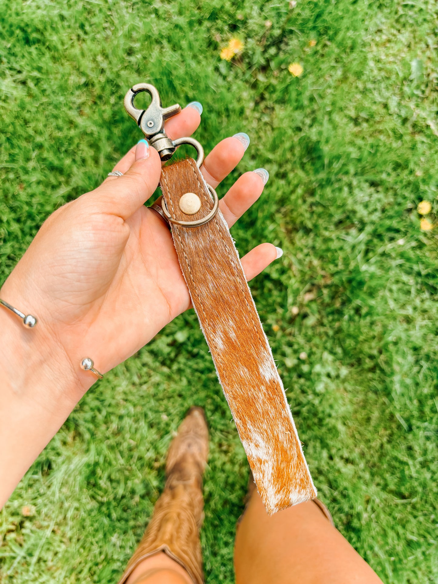 Western cowhide wristlet keychain accessory held by woman in cowboy boots – Hides & Kinds