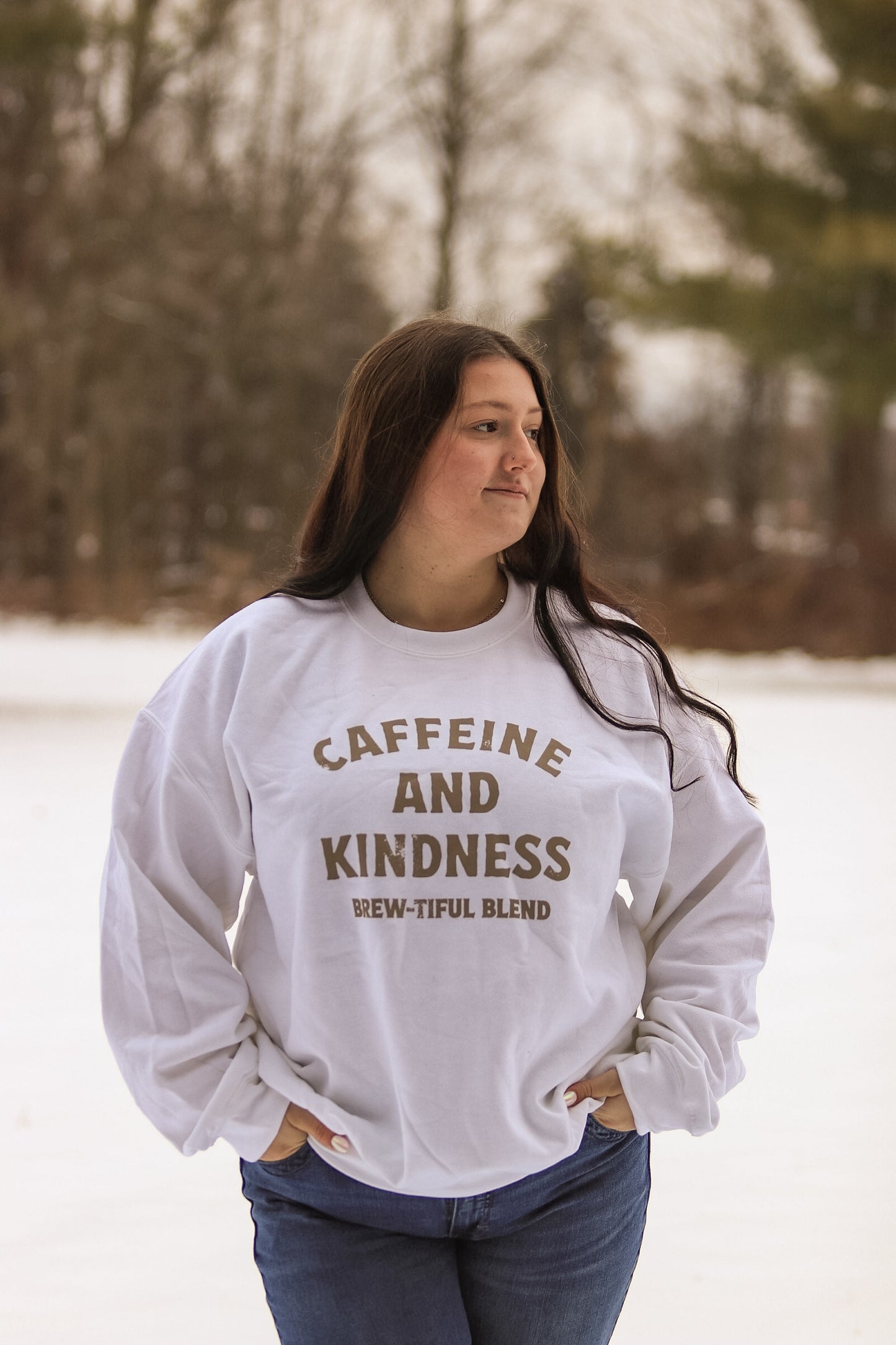 Full body view of a woman outdoors in winter wearing the Caffeine and Kindness white crewneck from Hides & Kinds.