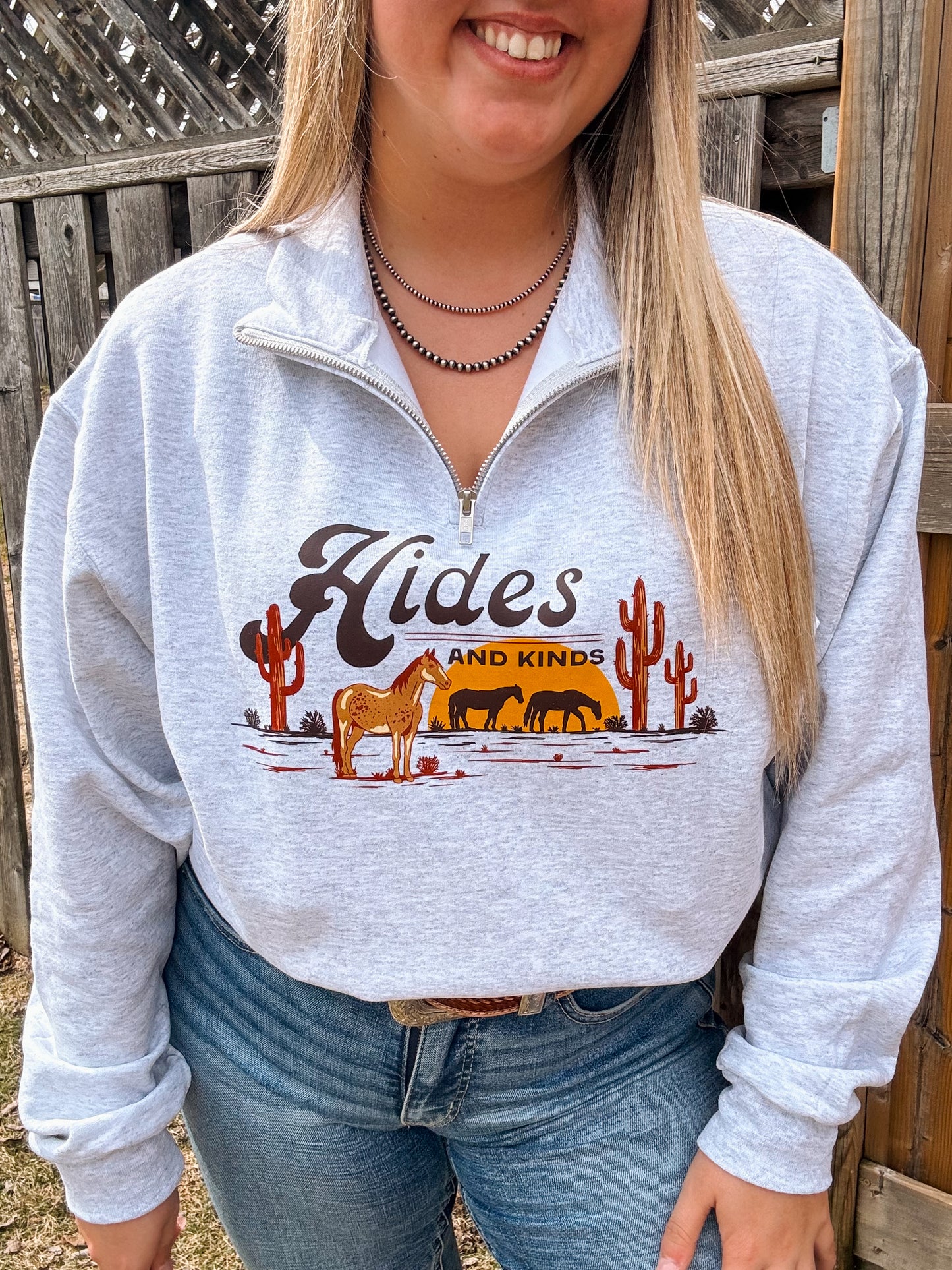 Model styled in the grey Desert Horse Quarter Zip by Hides and Kinds, featuring a desert scene with horses and cacti across the front.