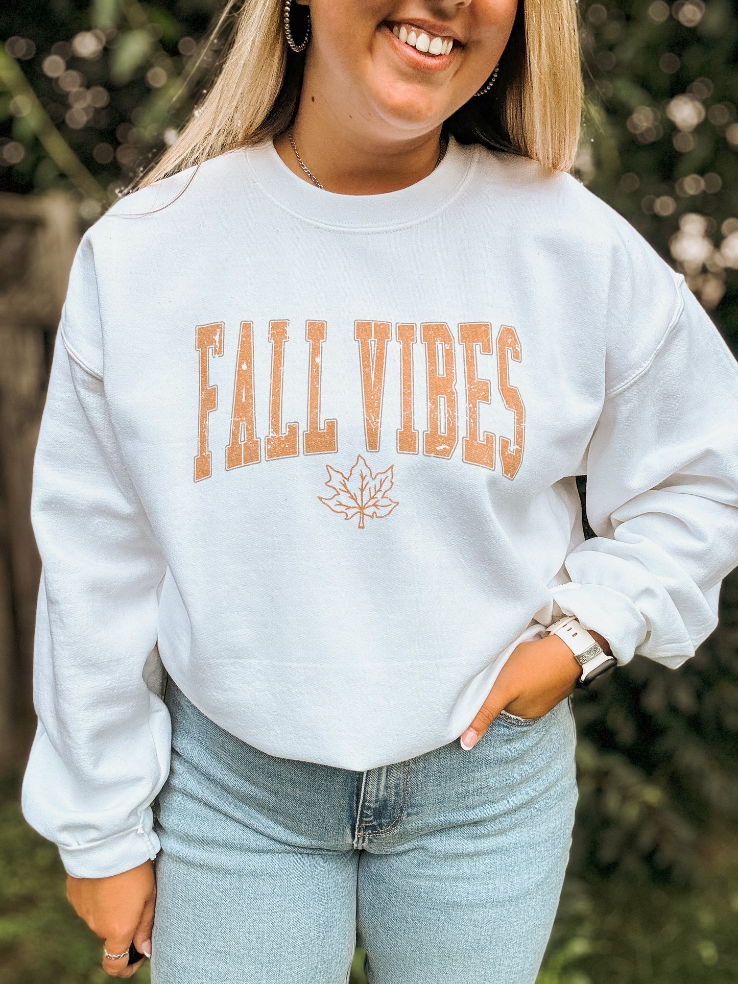 Close up of Fall Vibes graphic crewneck with maple leaf detail, worn tucked into jeans.