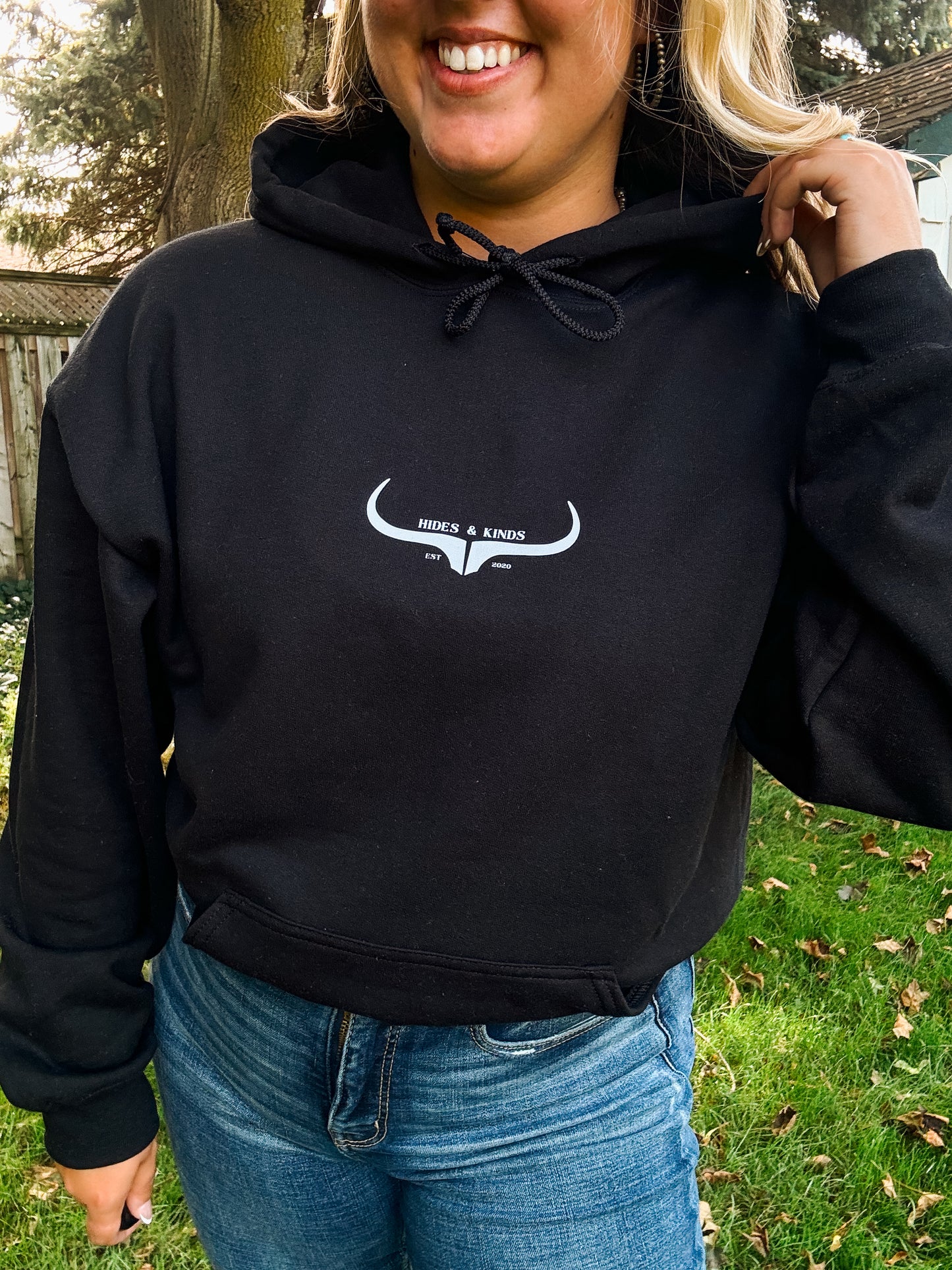 Close up of the black Hides and Kinds hoodie with original logo design, worn casually with jeans in a fall setting