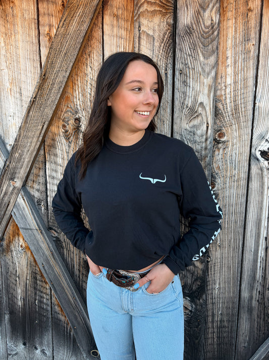 Person wearing a black sweatshirt with a logo, standing against a wooden background