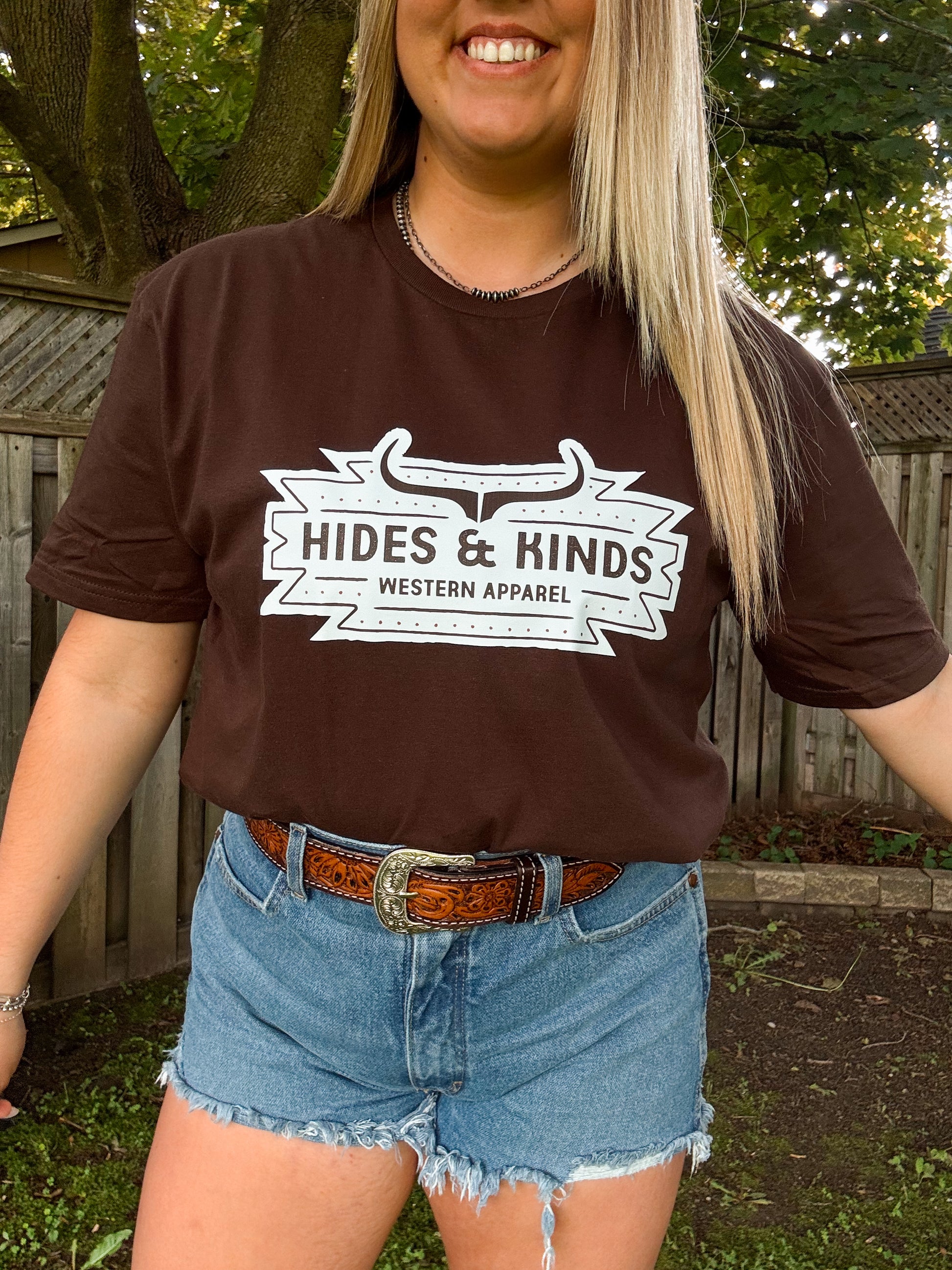 Close up of Hides and Kinds Aztec Badge Tee in chocolate brown with bold western logo and denim styling.