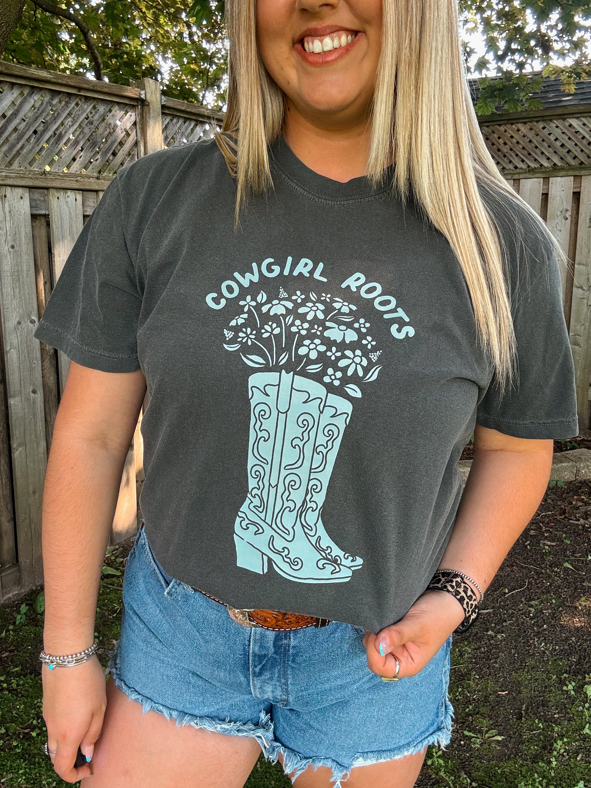 Close up of Cowgirl Roots Tee in pepper grey with light blue floral cowboy boots graphic by Hides and Kinds.
