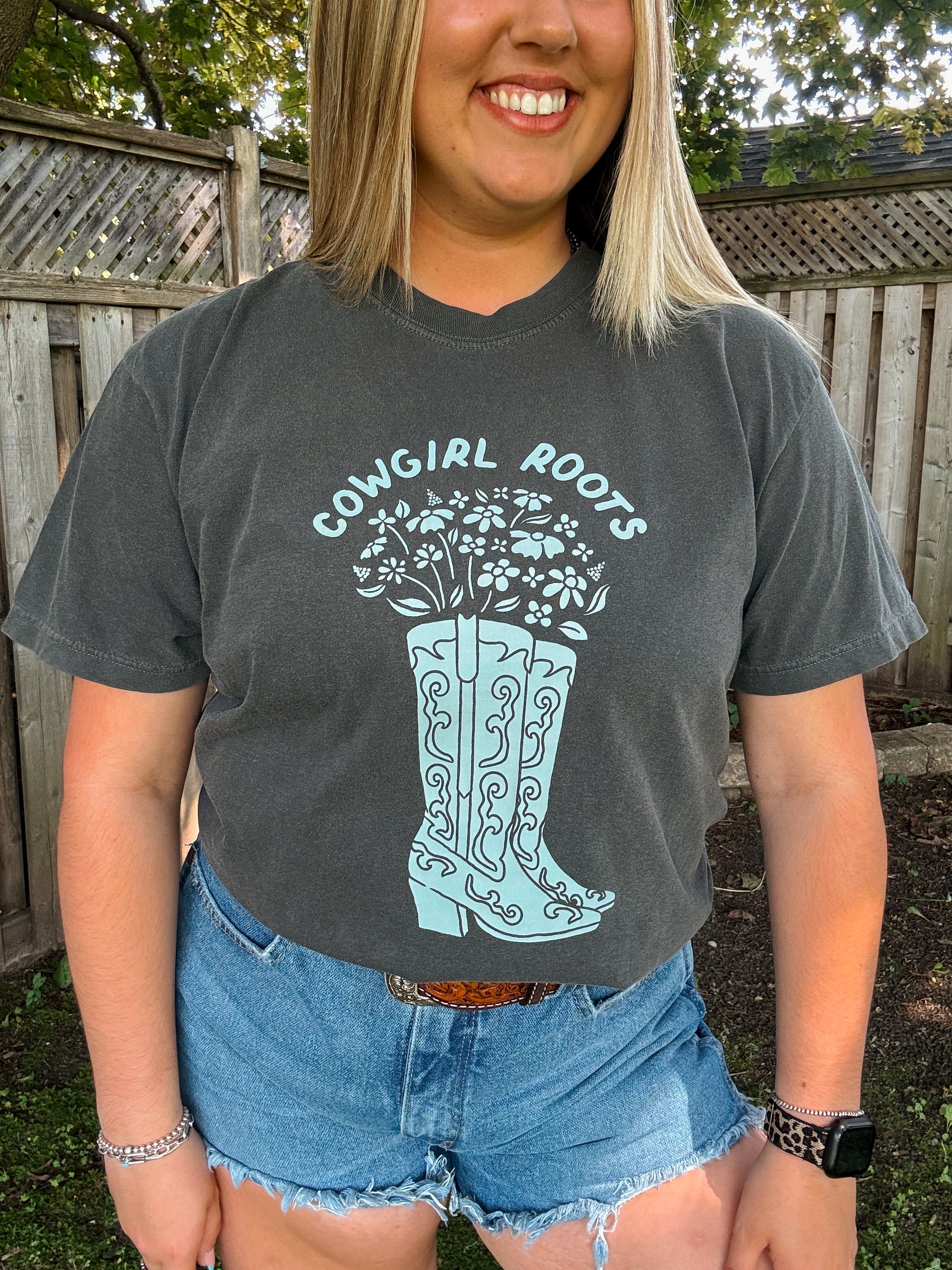 Front view of Cowgirl Roots t-shirt in pepper featuring light blue western boots and floral design.