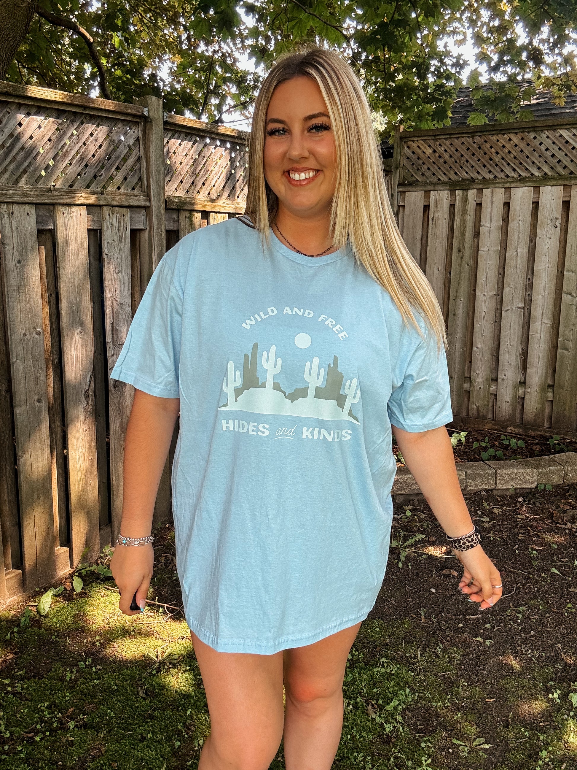 Smiling woman in oversized Wild and Free tee from Hides and Kinds, styled casually with silver jewelry.