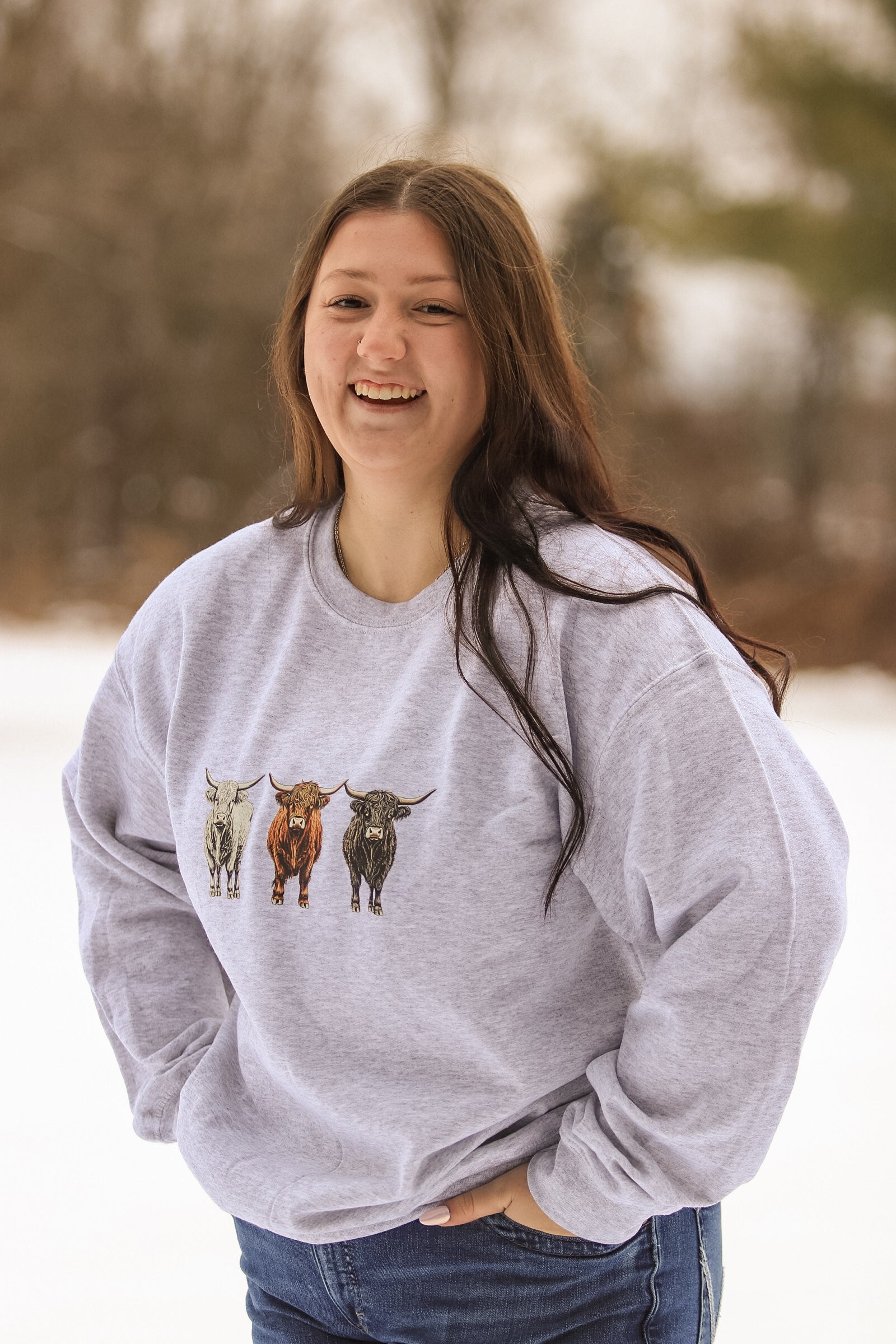 Side angle of model wearing Highland cow sweatshirt outdoors in winter.