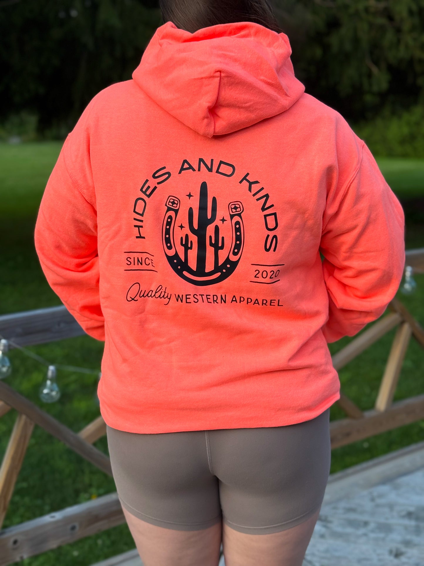 Back of coral Hides and Kinds hoodie featuring western horseshoe and cactus graphic with brand name.
