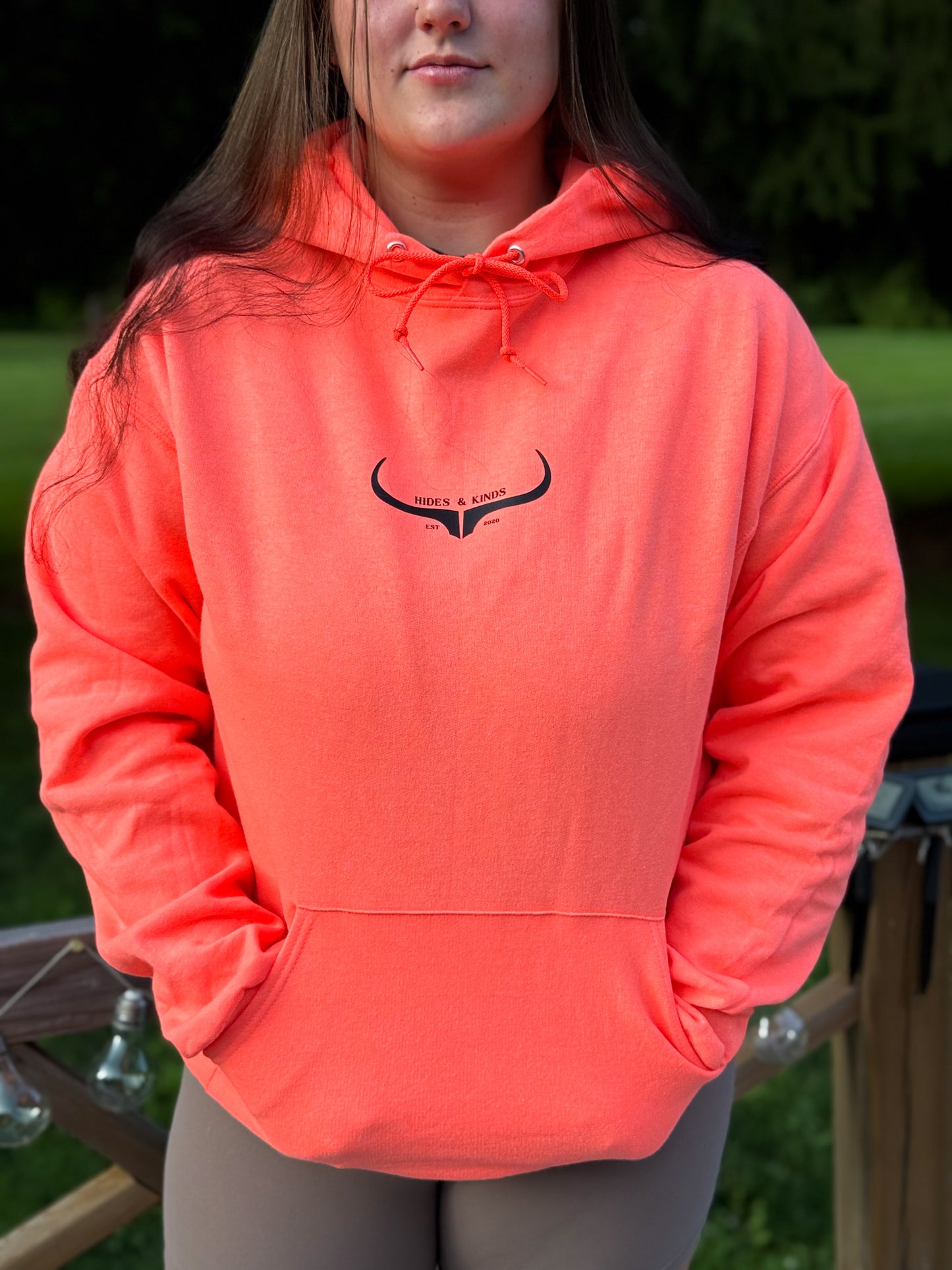 Woman wearing coral Hides and Kinds hoodie with minimalist longhorn logo on chest.