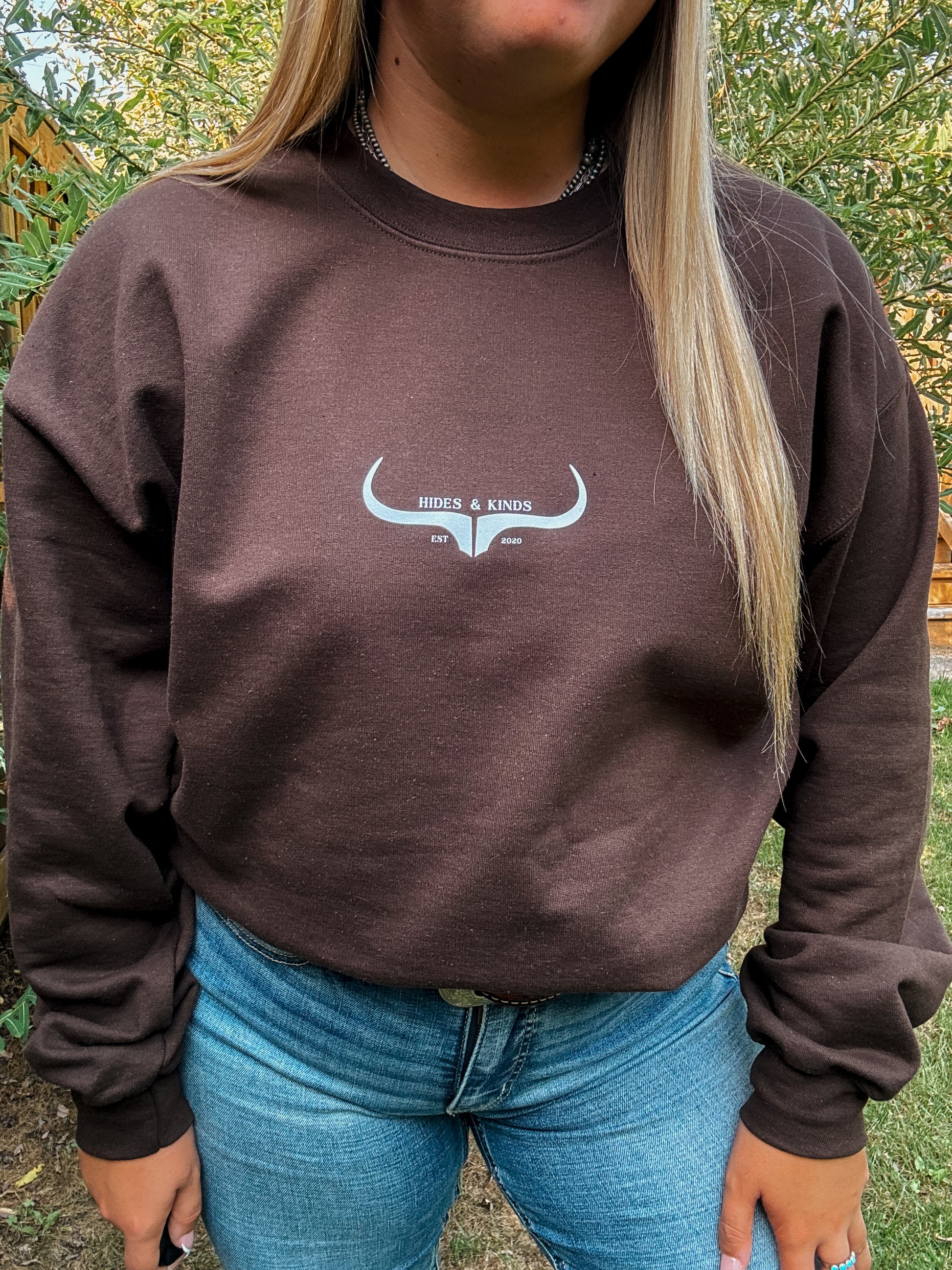 Close up view of Hides & Kinds Original Logo Crewneck in chocolate brown, featuring white steer head graphic and casual fit.