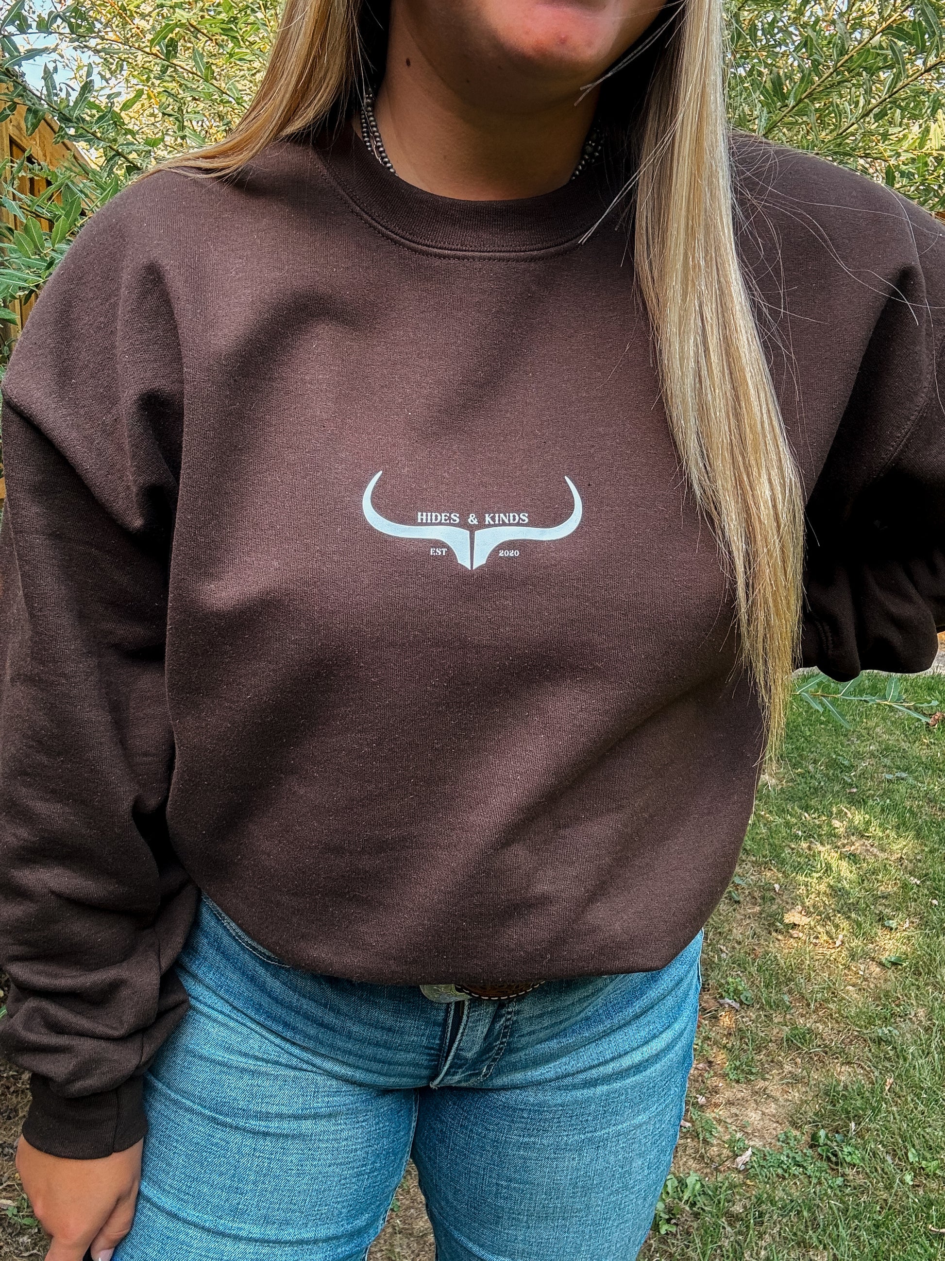Outdoor photo of Hides & Kinds chocolate brown crewneck sweatshirt with original logo and relaxed styling.