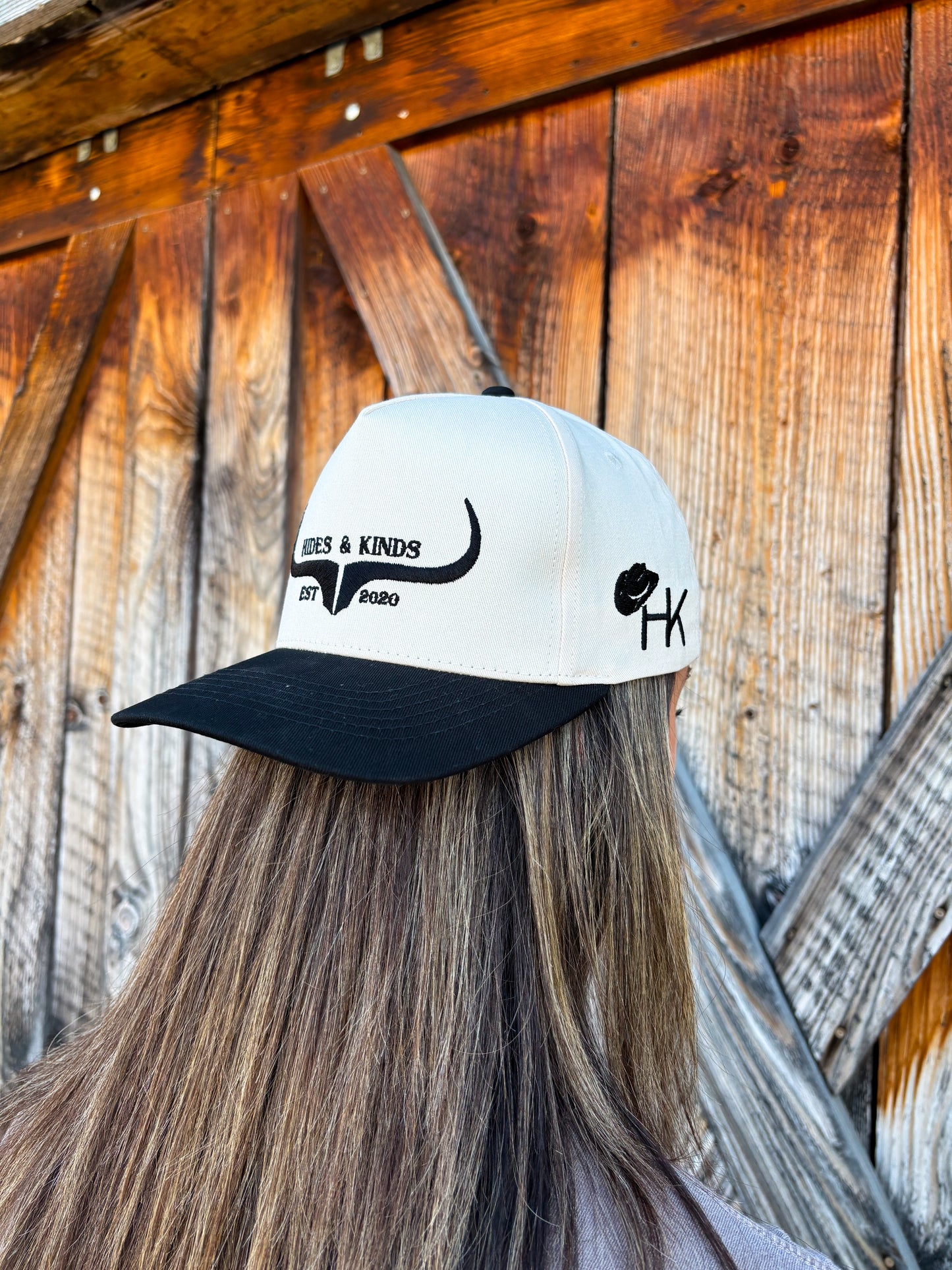 Side profile of the black and natural Hides & Kinds logo hat with HK and cowboy hat embroidery on the side panel.
