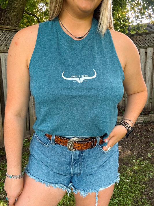 Close-up of teal Hides and Kinds sleeveless logo tank styled with denim cutoffs, silver jewelry, and a leather belt.