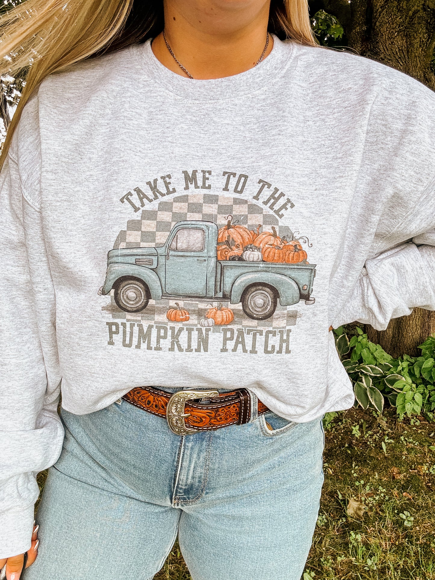 Woman wearing a grey crewneck sweatshirt with a vintage teal truck and pumpkins, reads "Take Me to the Pumpkin Patch" – cozy fall style by Hides & Kinds