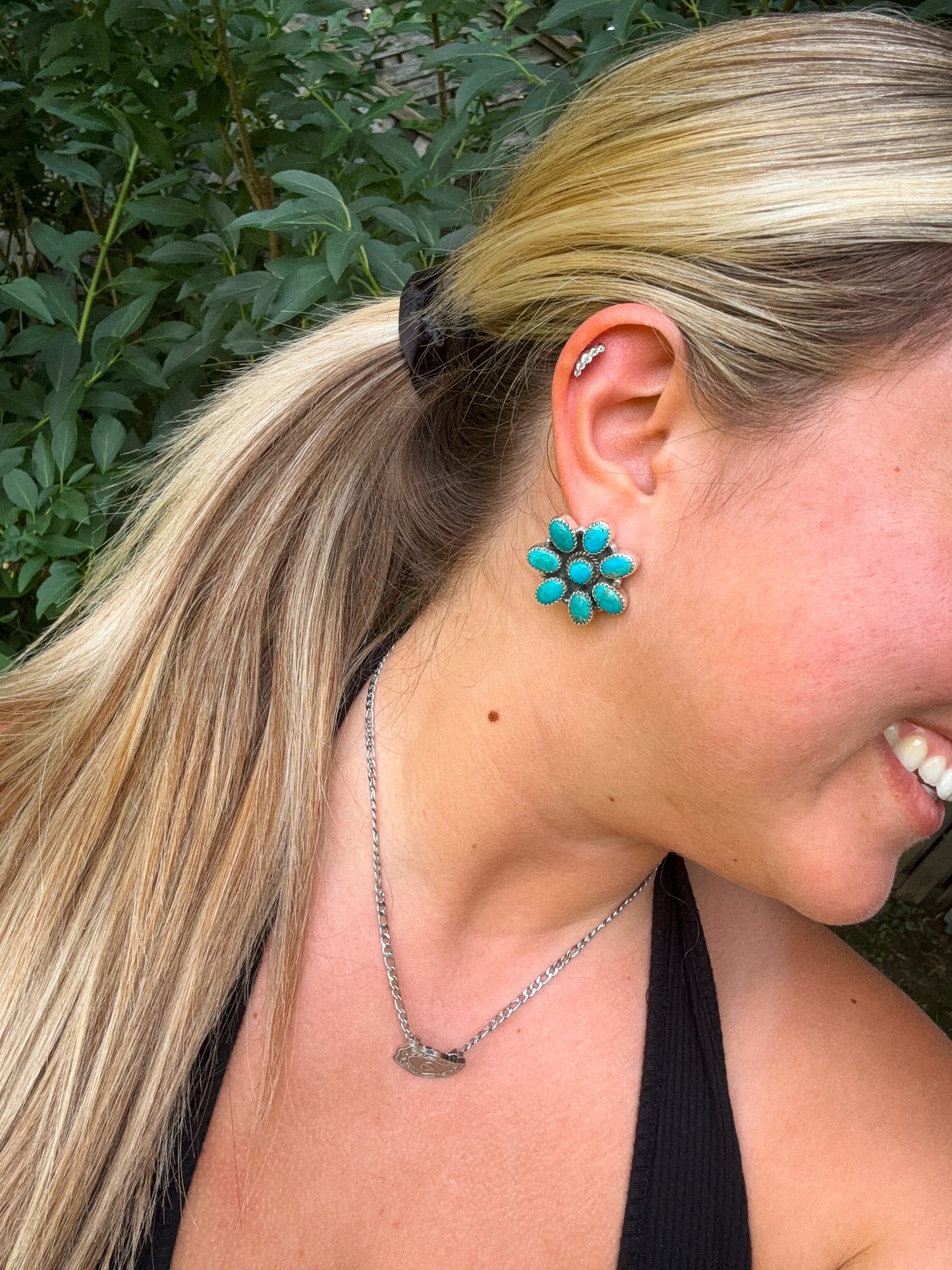 Close up of H&K turquoise flower stud earrings worn with a black tank top