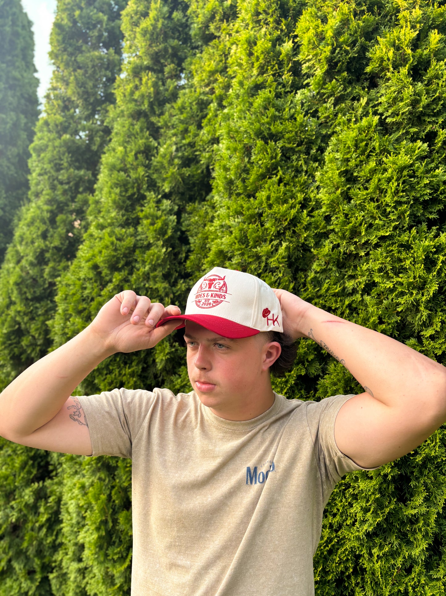 Man adjusting The Stampede Snapback hat outdoors wearing neutral tee.