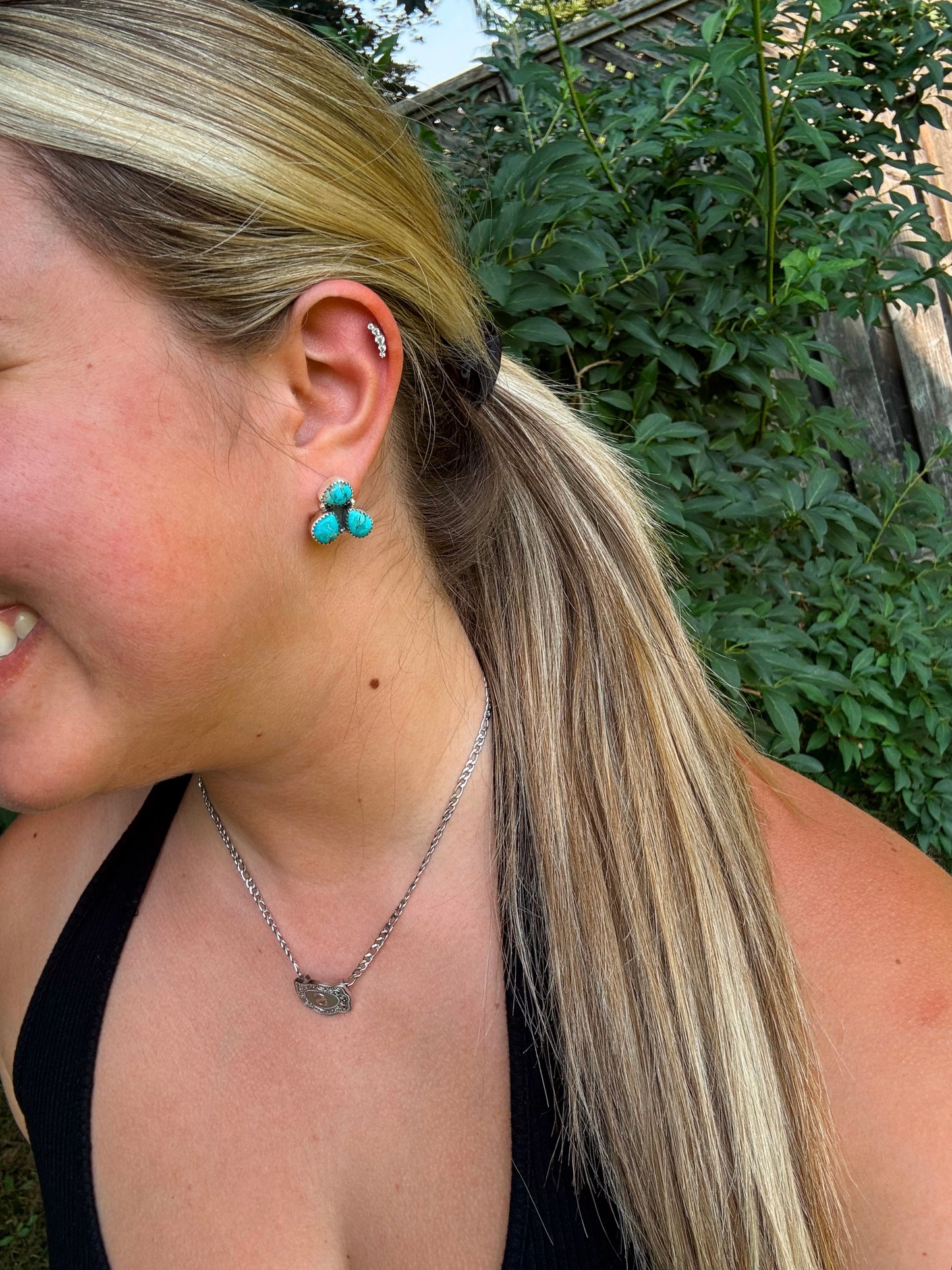 Close up of H&K Triple Stone Stud Earrings in turquoise worn with a black tank top outdoors