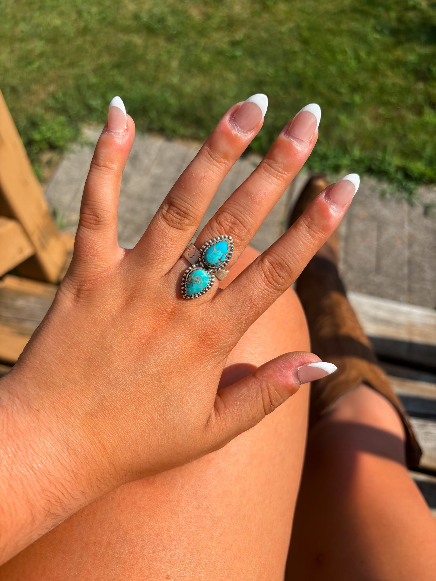 Close up of a hand wearing the Twin Trails Ring with two teardrop turquoise stones set in sterling silver.