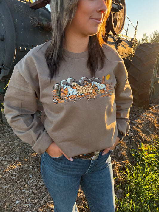 Detailed view of the Wild Run Crewneck showing galloping horses, cacti, a desert sunset and Hides & Kinds Western Co. lettering.