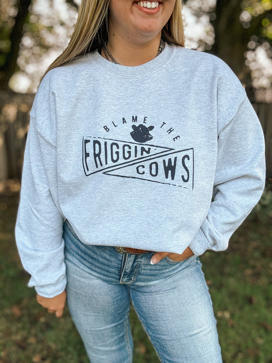 Model wearing the Blame the Cows Crewneck in athletic grey with western inspired text and cow graphic, styled with jeans and a concho belt.