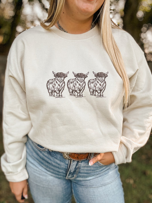 Sand crewneck sweatshirt with three hand drawn brown highland cows across the chest, styled with jeans and a western belt.
