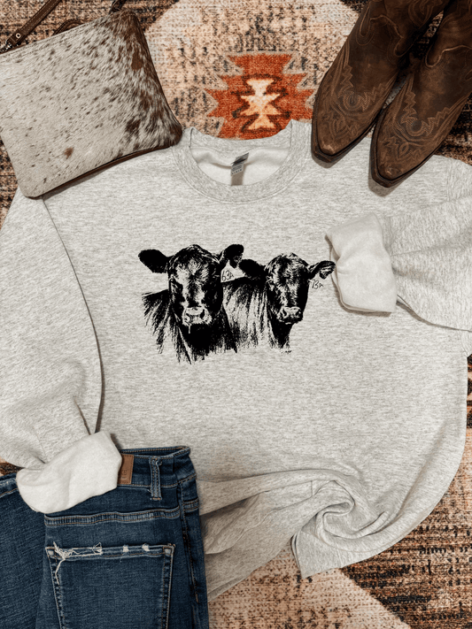 Heather grey crewneck with black cattle graphic, styled with denim, cowhide clutch, and western boots.