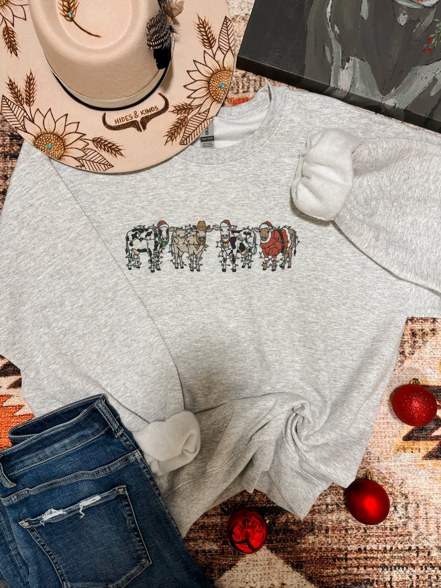 Heather grey Christmas cow graphic crewneck laid flat with holiday decor and jeans