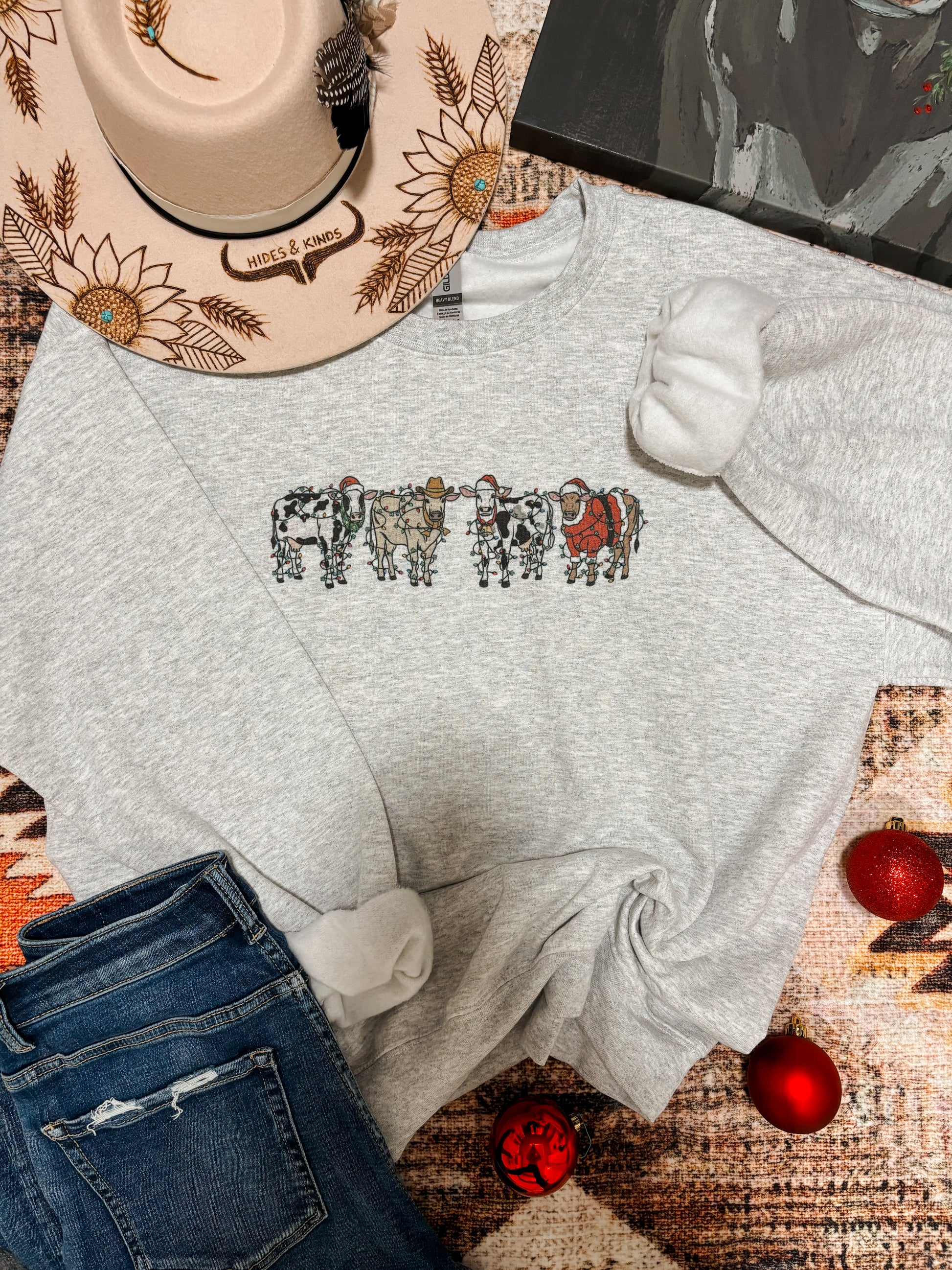 Heather grey Christmas cow graphic crewneck laid flat with holiday decor and jeans