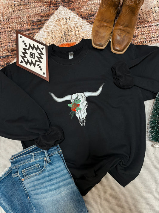 Western Christmas sweatshirt with a festive skull design, laid out beside cowboy boots, jeans, and a Southwestern boho print card.