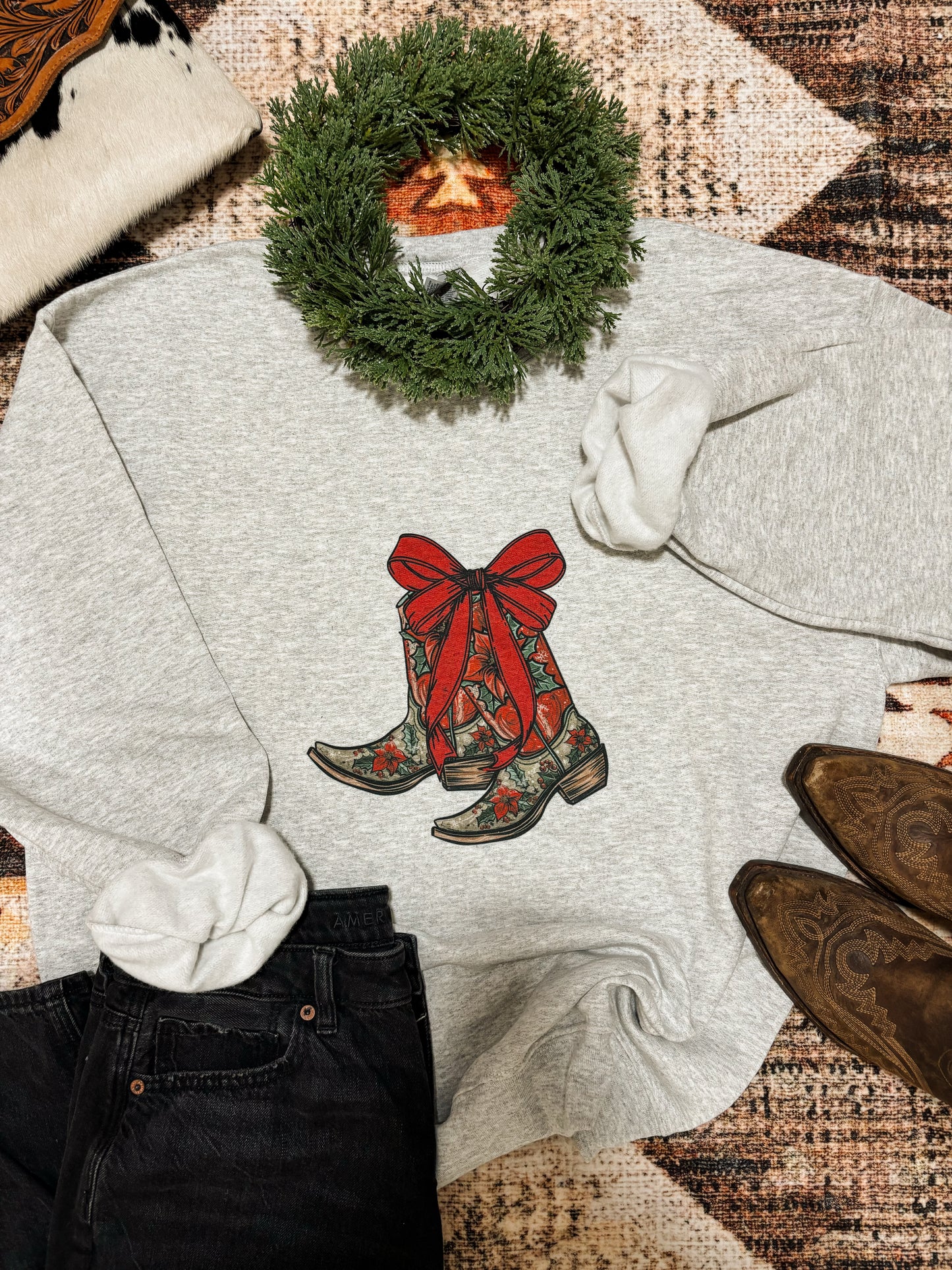 Cowgirl Christmas crewneck with festive cowboy boots graphic and red bow, styled with jeans and boots