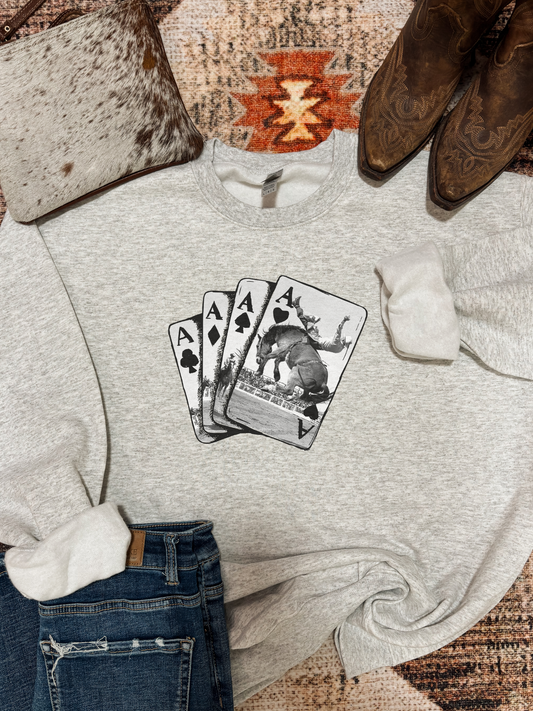 Hides and Kinds Ace of Spades crewneck with western poker card graphic laid out with jeans, boots, and cowhide clutch