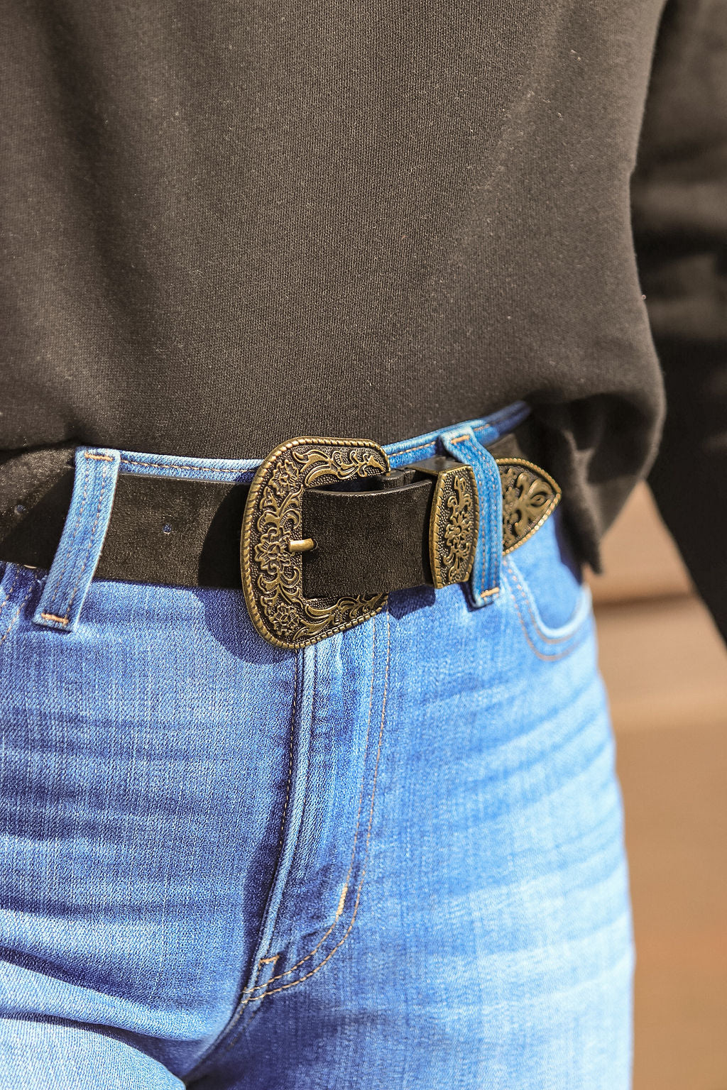 Close up of antique gold engraved buckle on black suede western belt