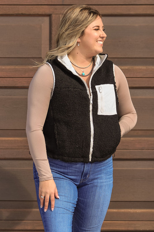 Front view of women’s black fleece vest with white zipper and chest pocket from Hides & Kinds.