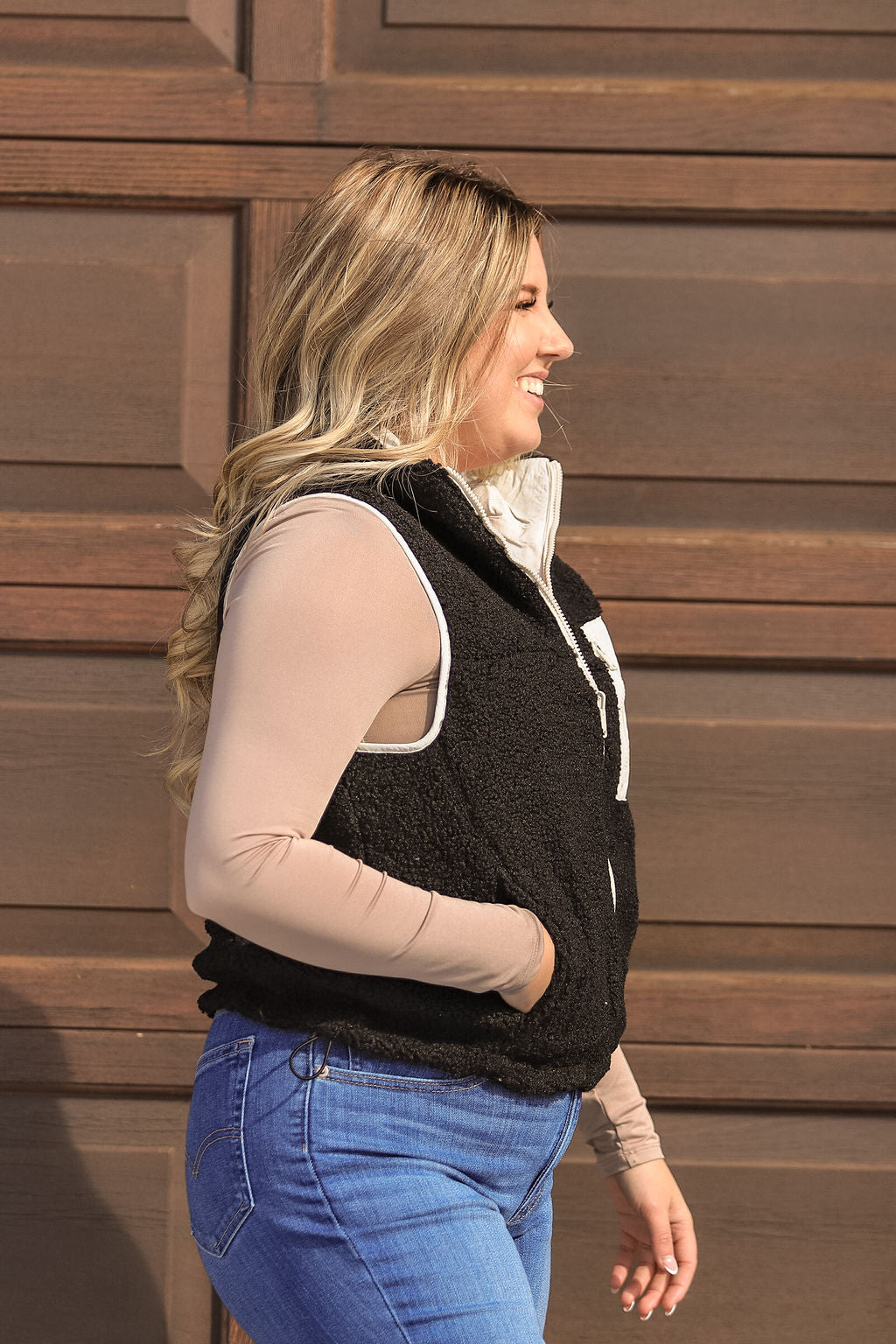 Side view of women’s black fleece vest with contrast white zipper and pocket, styled with jeans.
