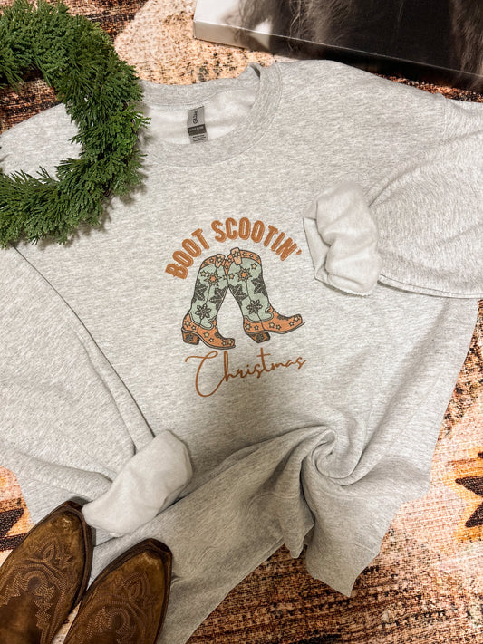 Christmas cowgirl sweatshirt with boot graphic and wreath accent, laid flat on western rug