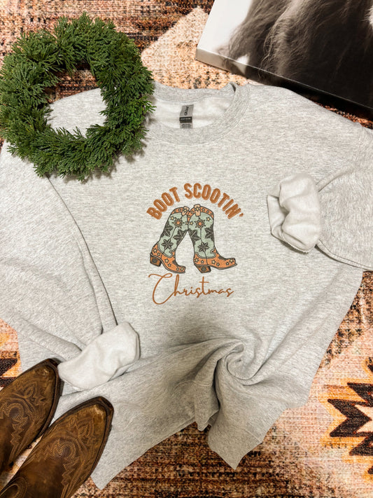 Light grey crewneck with colorful western boots and “Boot Scootin’ Christmas” graphic, styled with cowboy boots and wreath