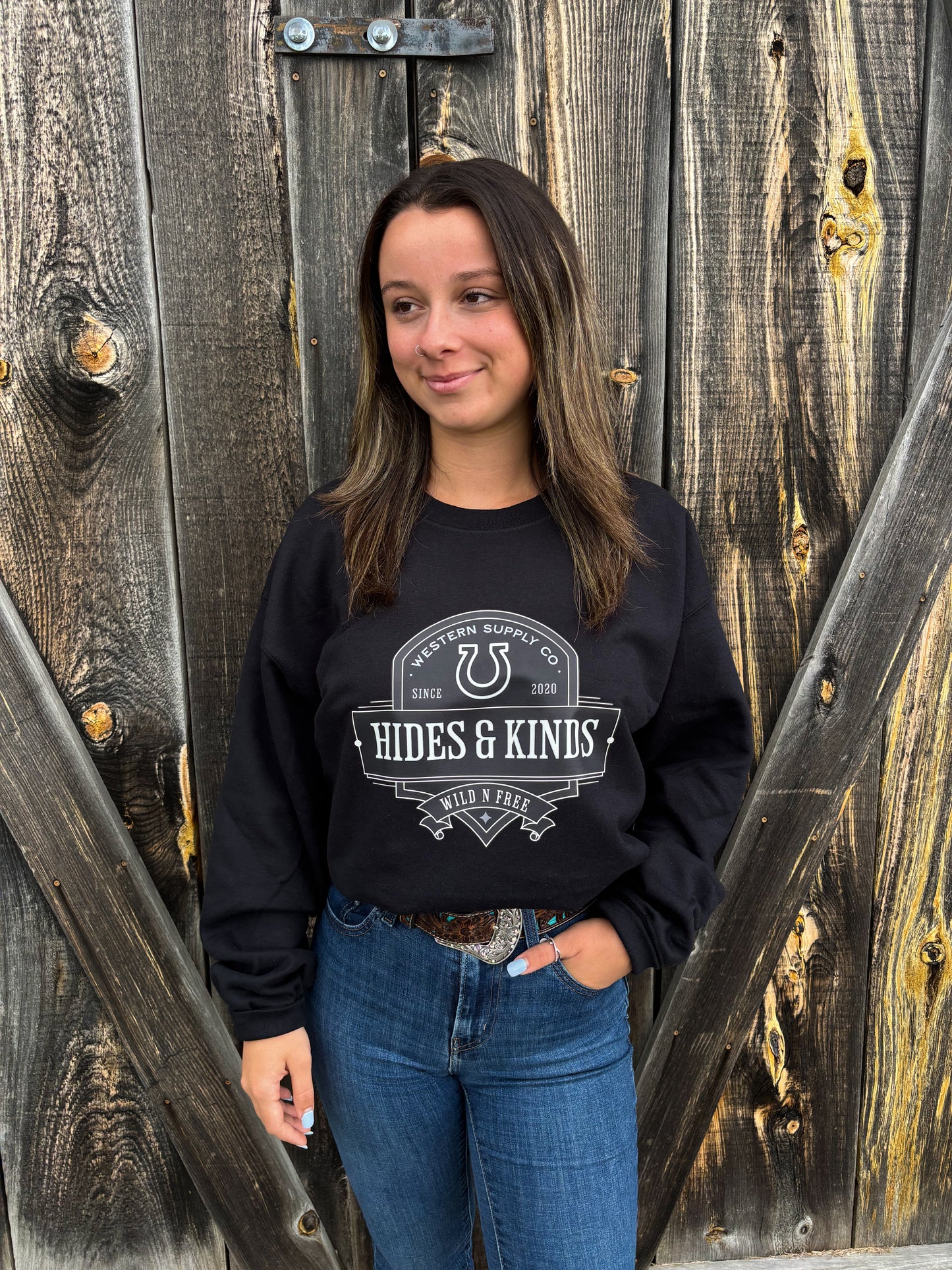Smiling woman in the black Hides & Kinds Outback Crewneck against barnwood backdrop