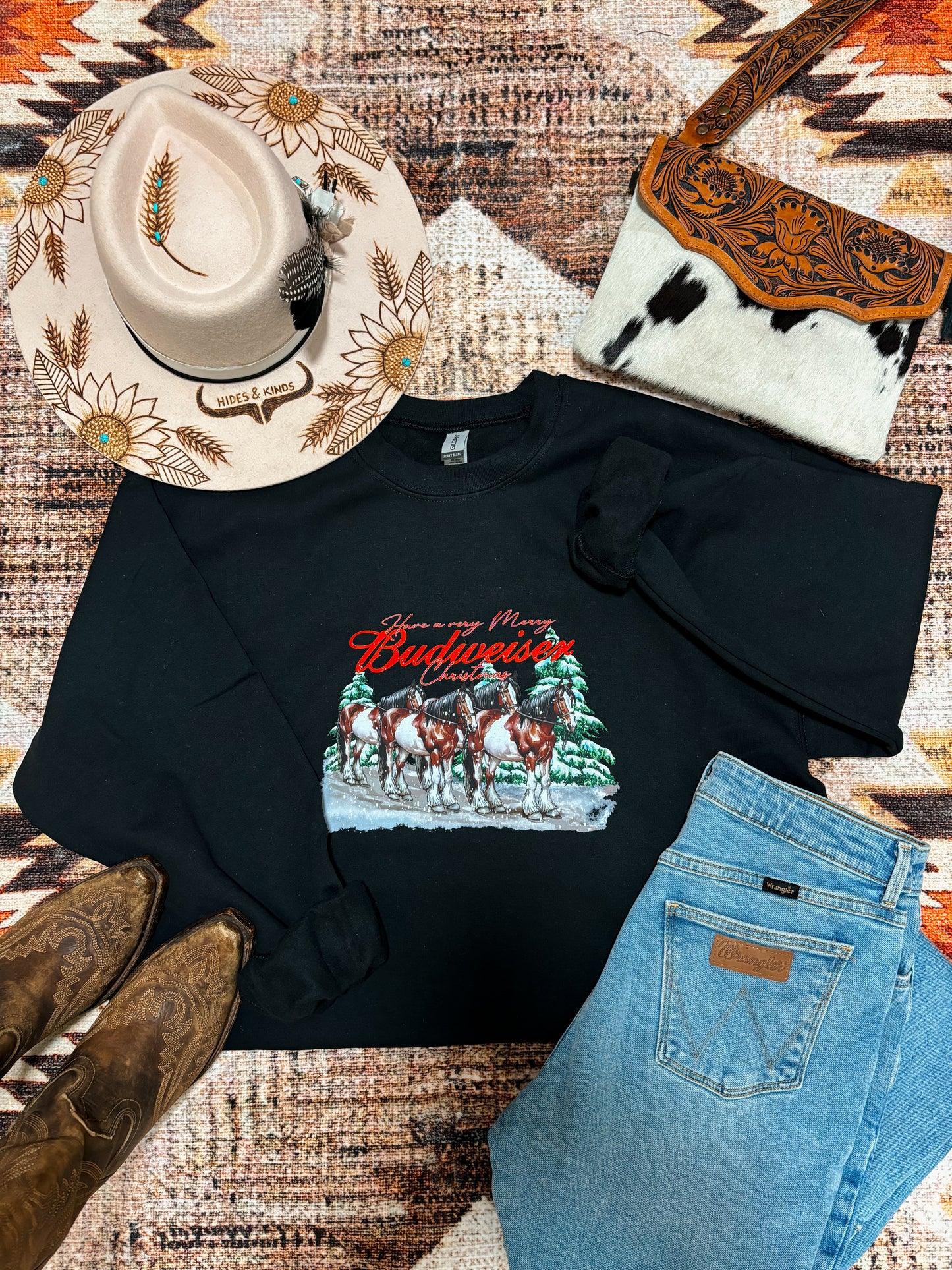 Festive western outfit featuring Budweiser Christmas crewneck, embroidered cowboy hat, leather cowhide purse, and Wrangler jeans.