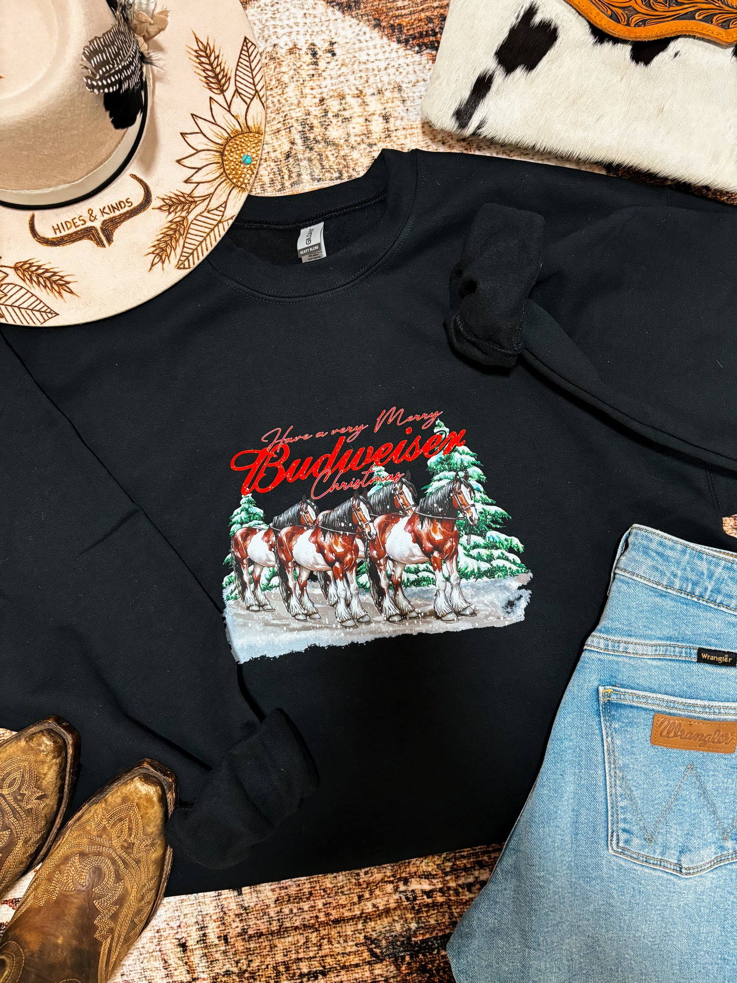 Close up flat lay of black Budweiser Christmas crewneck with Clydesdale horse graphic and rustic western holiday styling.