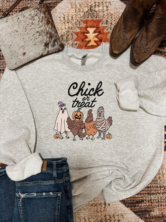 Grey crewneck featuring four cartoon chickens dressed in Halloween costumes with pumpkins and “Chick or Treat” text, styled with jeans, cowhide purse, and western boots
