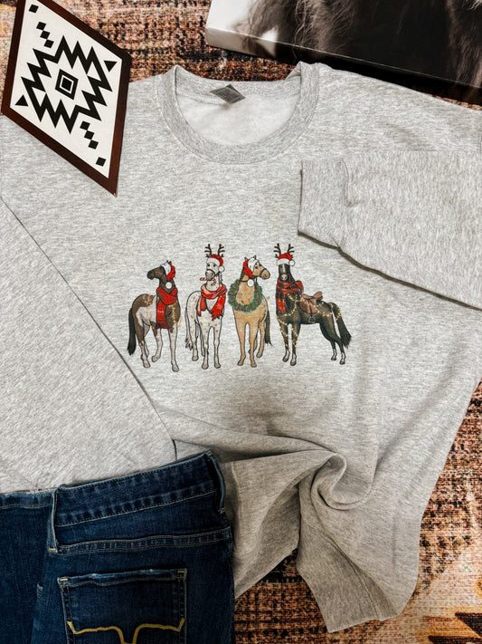 Christmas Horses crewneck sweatshirt in ash grey with five festive horses wearing western holiday gear, styled with jeans on a rustic background