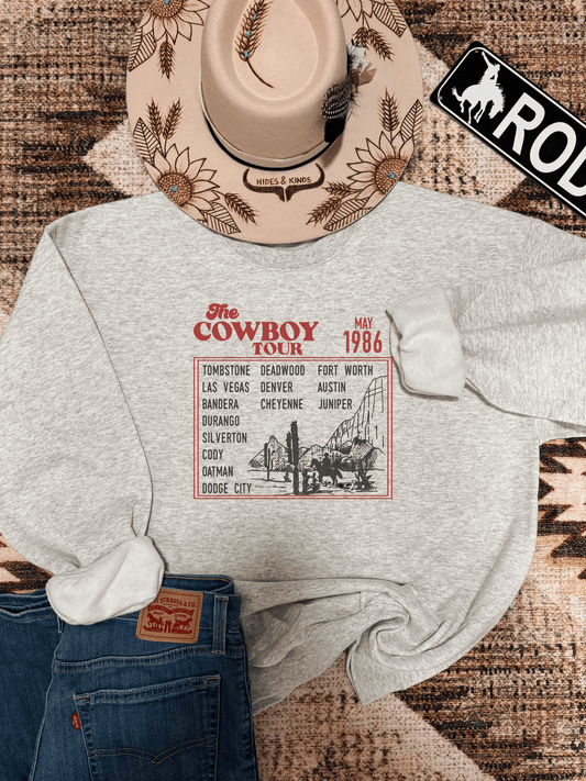 Ash grey Cowboy Tour crewneck from Hides & Kinds featuring vintage western cities graphic and rustic flat lay styling with hat and jeans