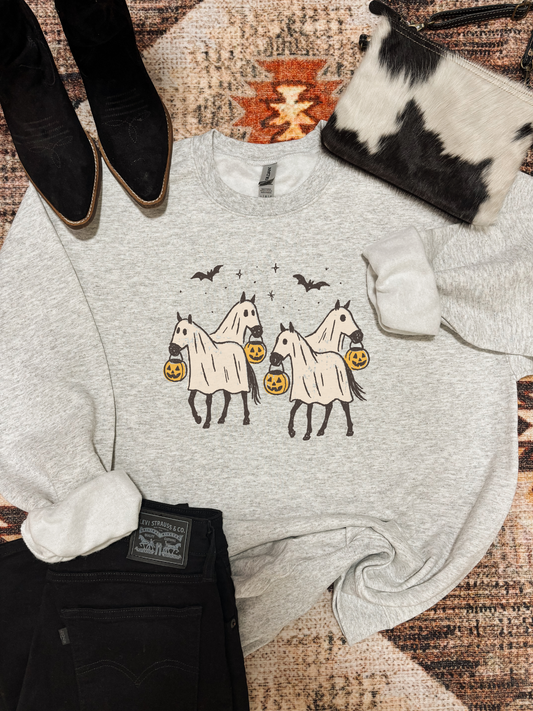 Light grey crewneck with three ghost horses holding pumpkins, styled with black boots, cowhide purse, and black Levi’s jeans on a western rug