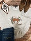 Hides and Kinds Jingle Horse crewneck sweatshirt laid out with cowboy boots, western decor, and denim jeans