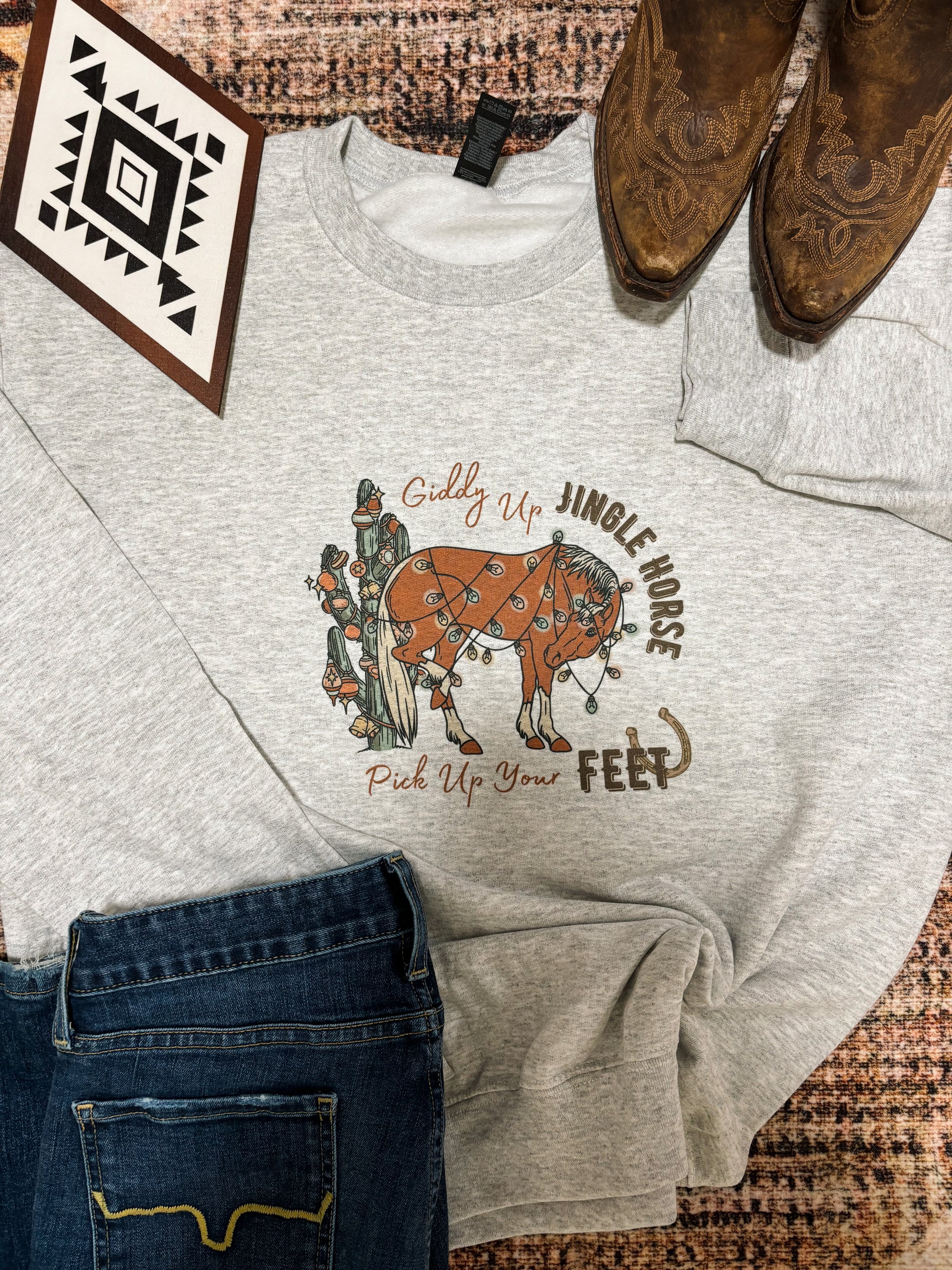 Western themed flatlay of Jingle Horse crewneck with vintage cowboy boots and aztec artwork
